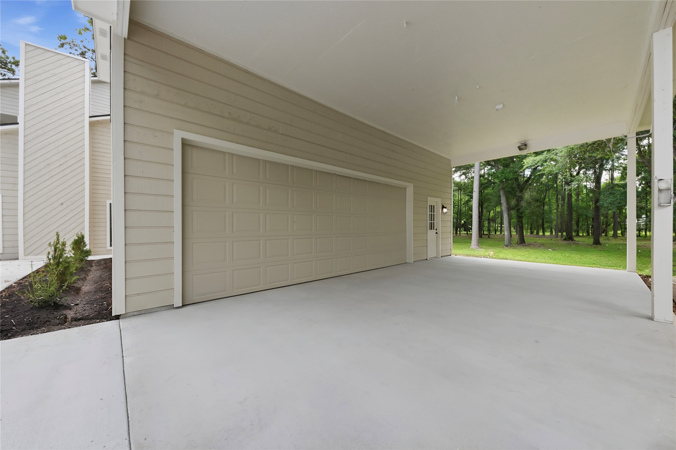 Exterior view of the detached 3-car garage structure showing oversized garage door, fresh concrete drive, board-and-batten siding, and direct access to the surrounding 1.67 acres of wooded land. Easy turnaround and ample parking.
