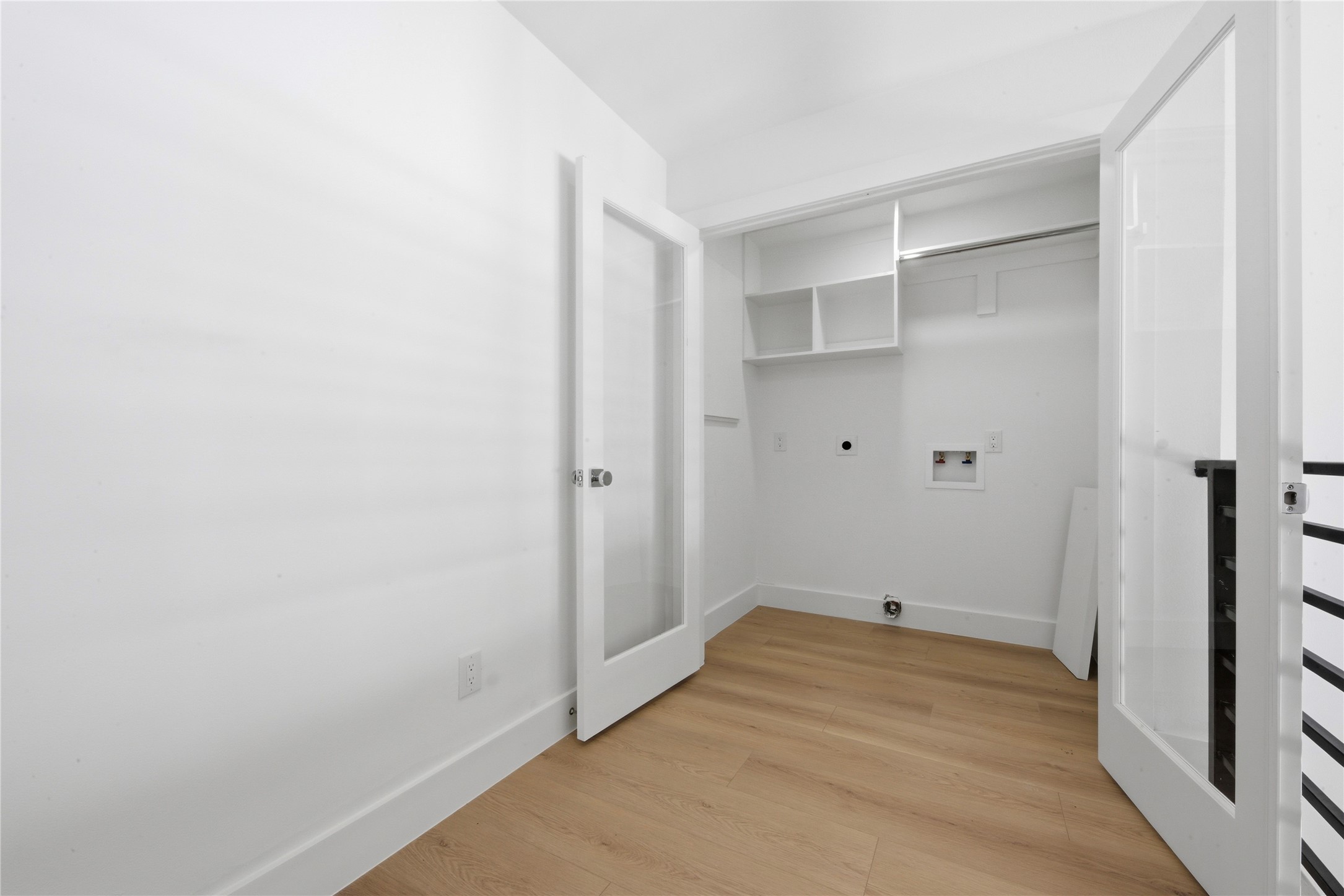 Bright second-floor utility room with washer/dryer hookups, built-in shelving, recycled-glass French doors, and wide-plank floors. Convenient placement near the secondary bedrooms.