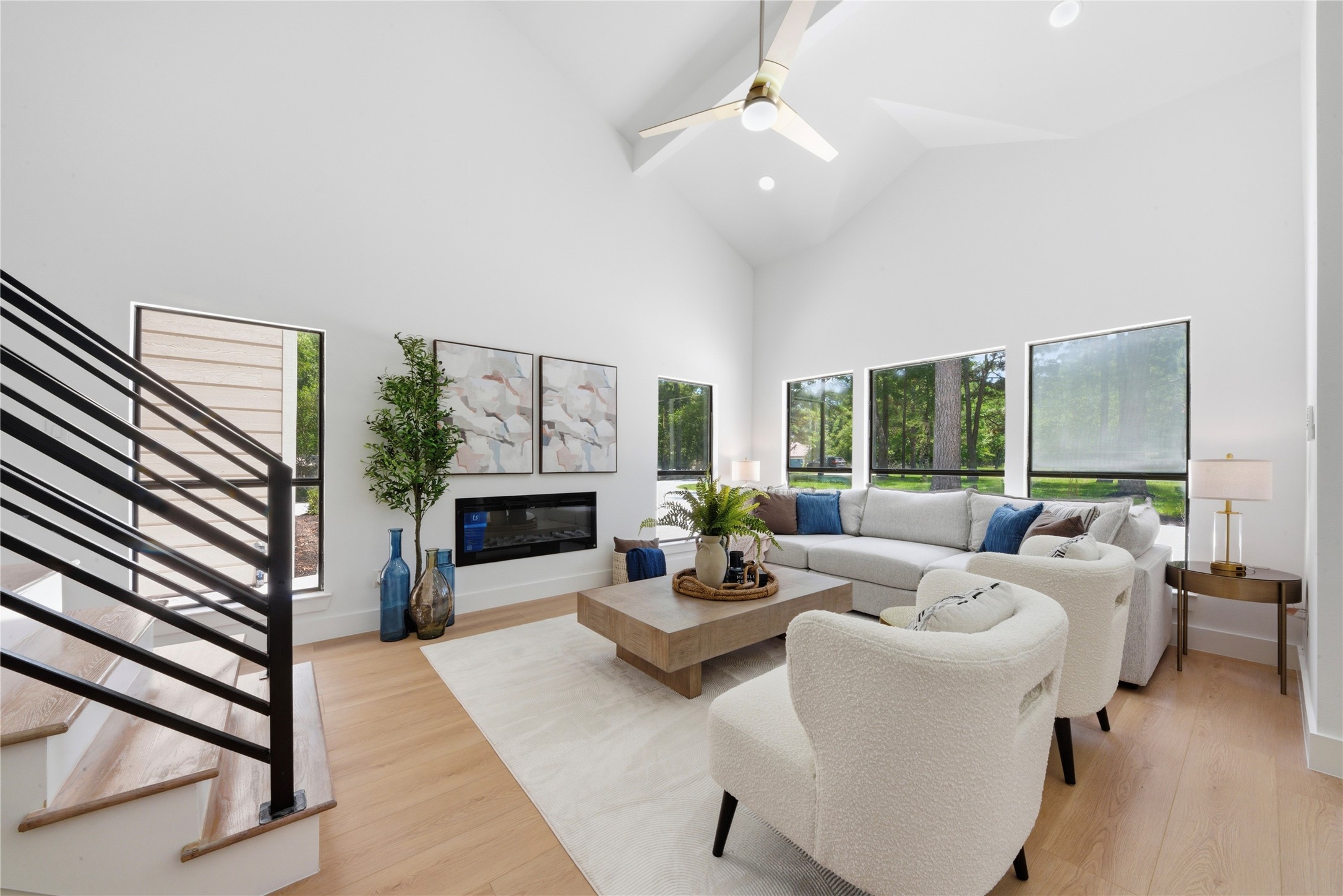Light-filled great room with vaulted 20-ft ceilings, linear fireplace, and panoramic wooded views. Designer ceiling fan, recessed lighting, and oversized windows fill the space with natural light. Luxury vinyl floors flow throughout.