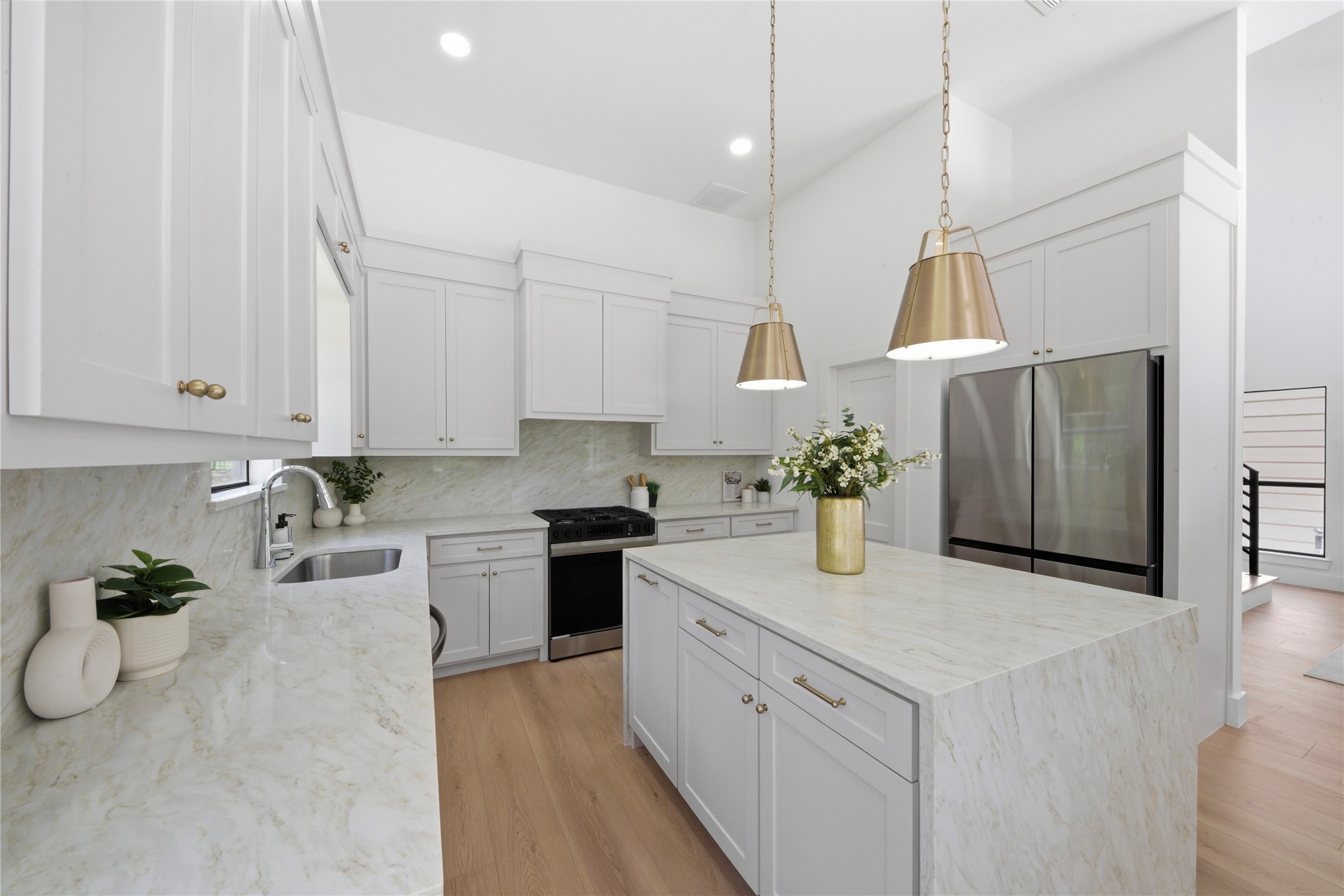 Designer chef's kitchen featuring oversized waterfall quartz island, custom cream shaker cabinetry, brass cone pendants, stainless steel appliances, gas range, and quartz slab backsplash. Light wide-plank floors and brass hardware throughout.