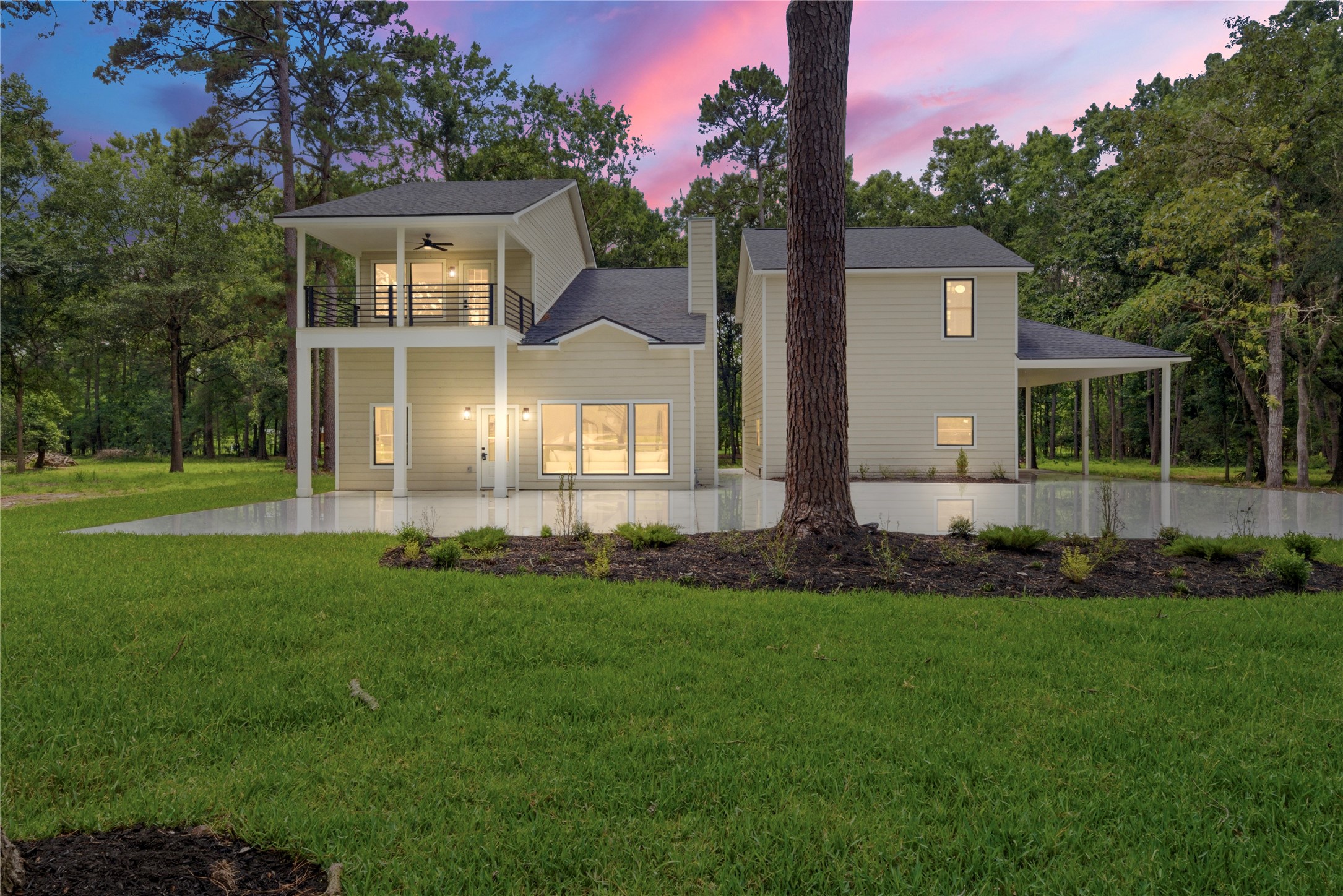 Stunning twilight view of this 3,243 SF modern farmhouse on 1.67 wooded acres in Cimarron Country. Two-story design with covered upper balcony, board-and-batten siding, and detached 3-car garage with room to the right.