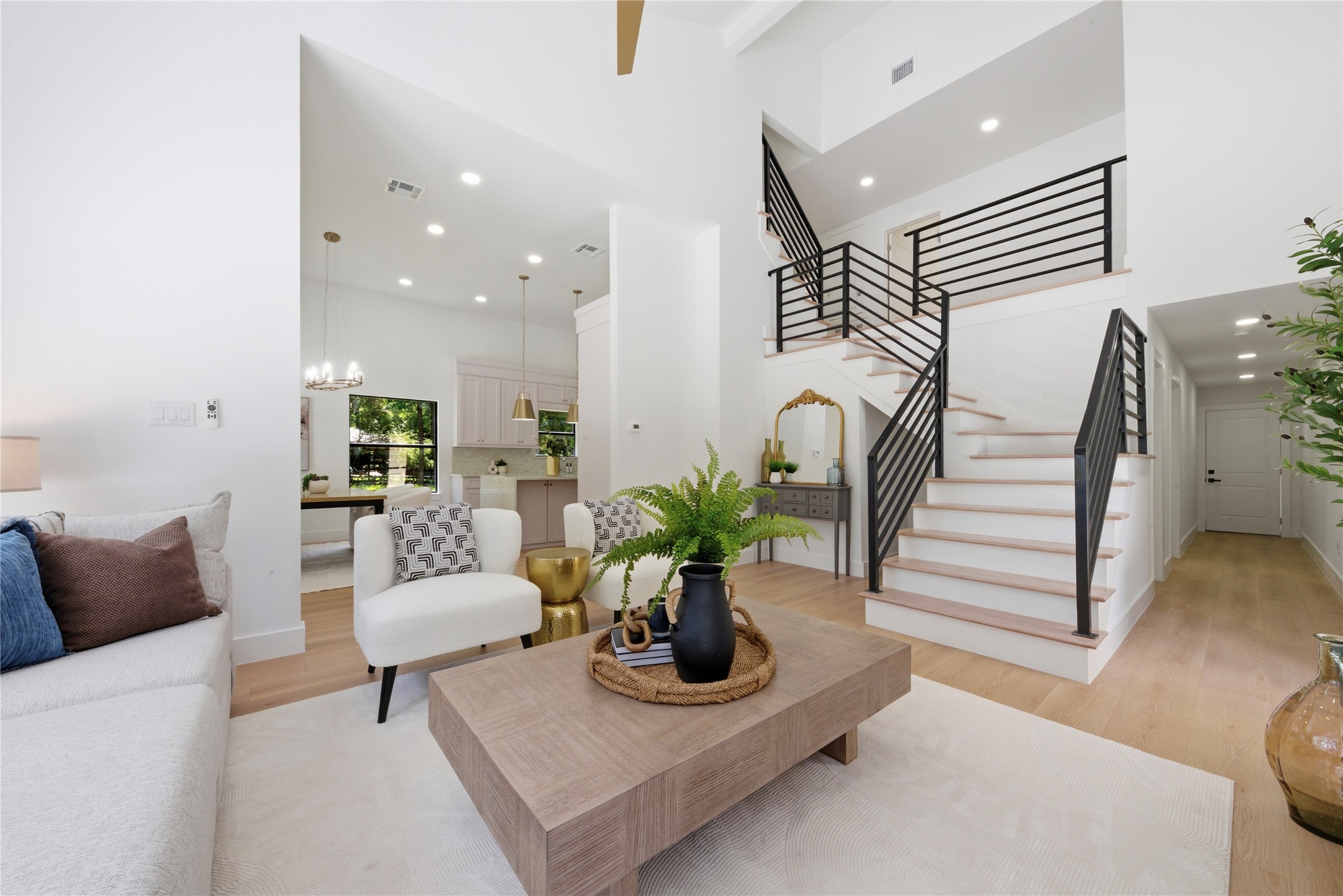 Dramatic entry showcasing the architectural floating steel staircase, soaring ceilings, and views into the kitchen and dining area. White oak treads and horizontal black metal rail create a contemporary statement.