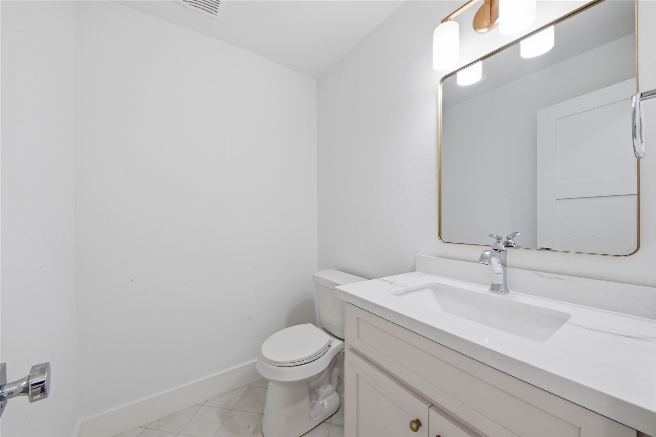 Elegant powder bath featuring custom vanity with quartz counter, brass-framed mirror, designer brass sconce lighting, and tile flooring. Conveniently located on the main floor.