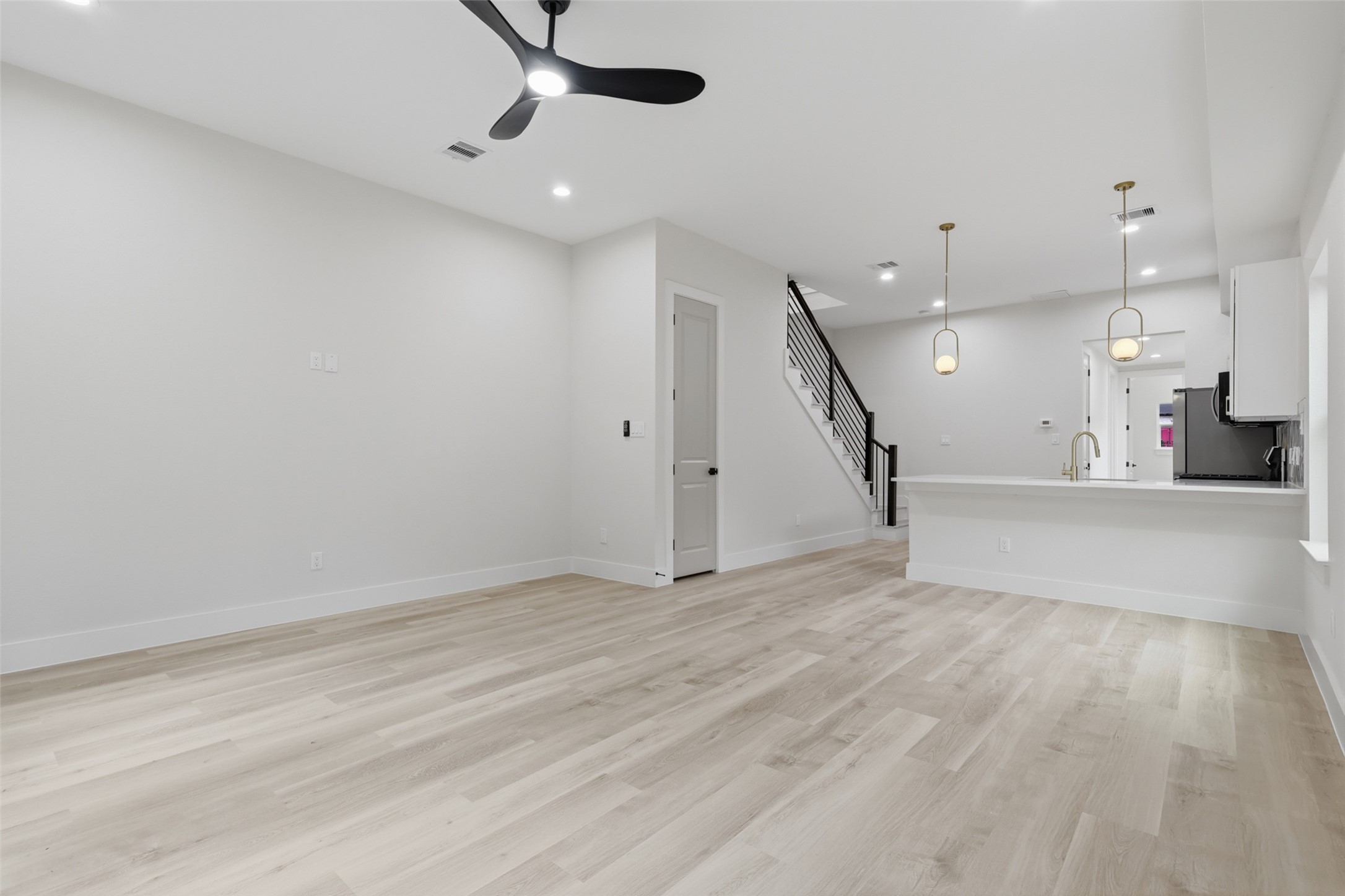 Spacious open-concept living area featuring sleek light LVP flooring, modern ceiling fan, and elegant pendant lighting over a stylish kitchen.