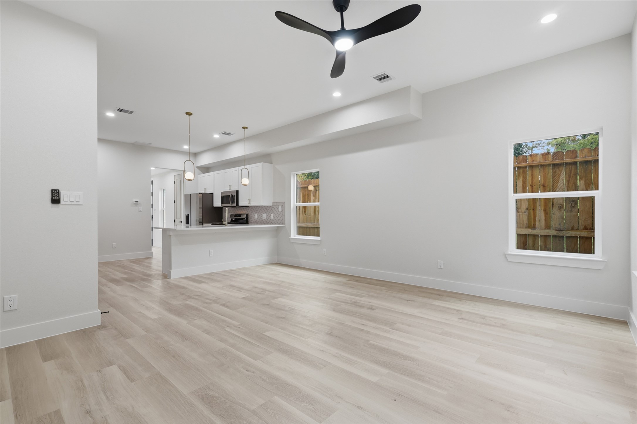 Spacious open-concept living area with sleek LVP flooring, modern ceiling fan, and abundant natural light, seamlessly flowing into a contemporary kitchen with stylish pendant lighting and stainless steel appliances.