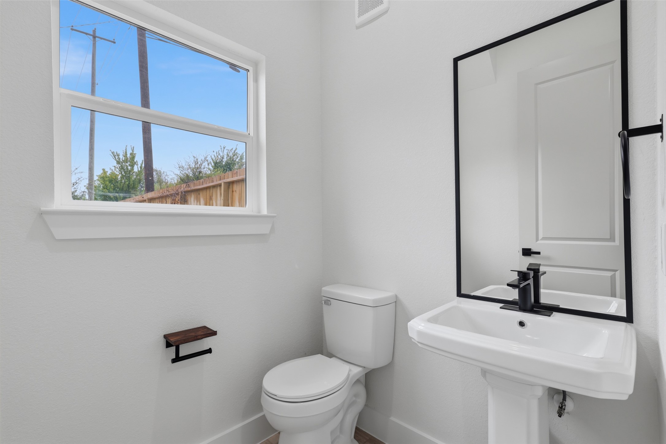 Bright and modern 1,2 bath in the front entrance on the first floor, featuring a sleek pedestal sink, large mirror, and natural light streaming through the window.