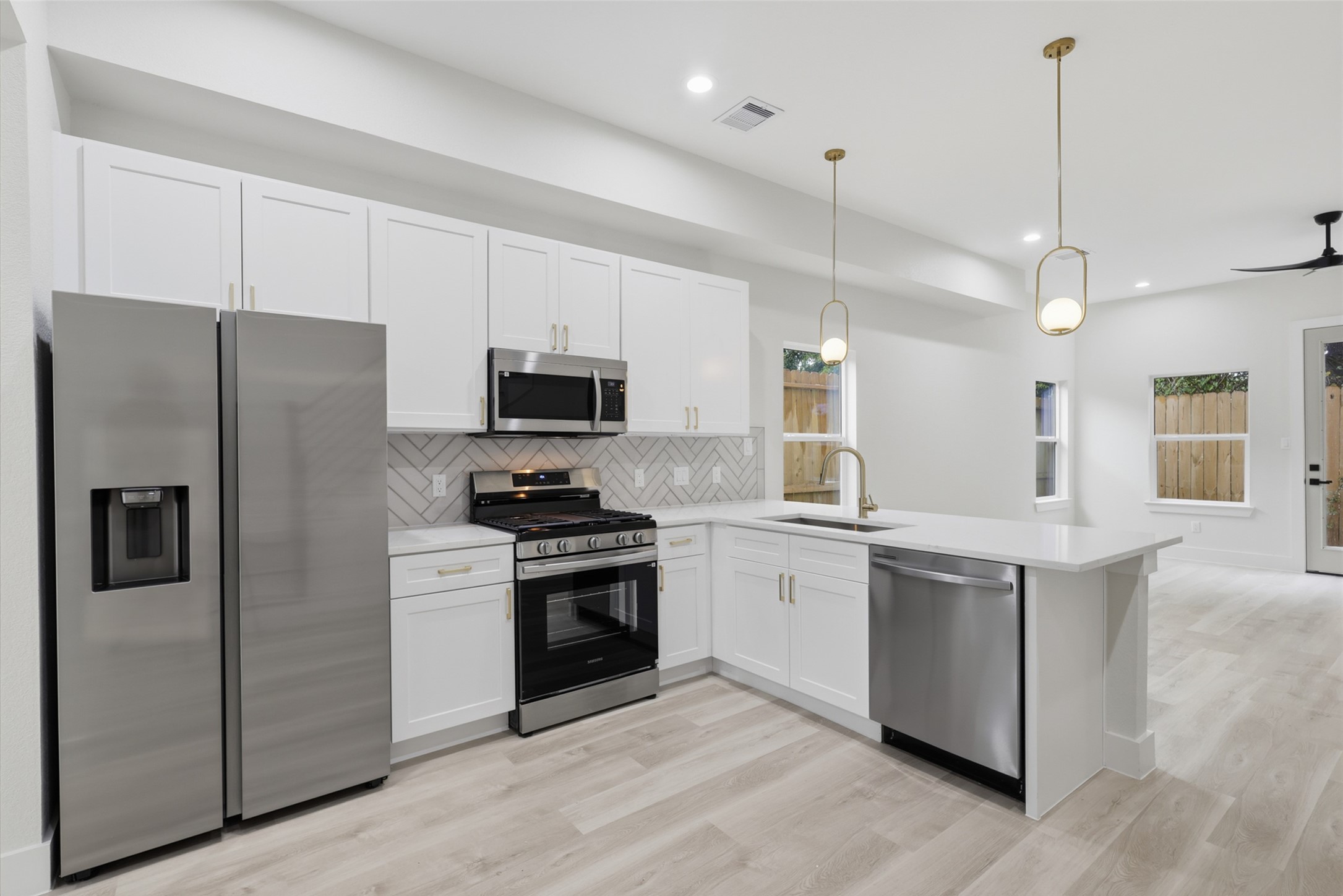 Sleek modern kitchen featuring stainless steel appliances, elegant white cabinetry, and a spacious L-shaped island with pendant lighting, perfect for entertaining.