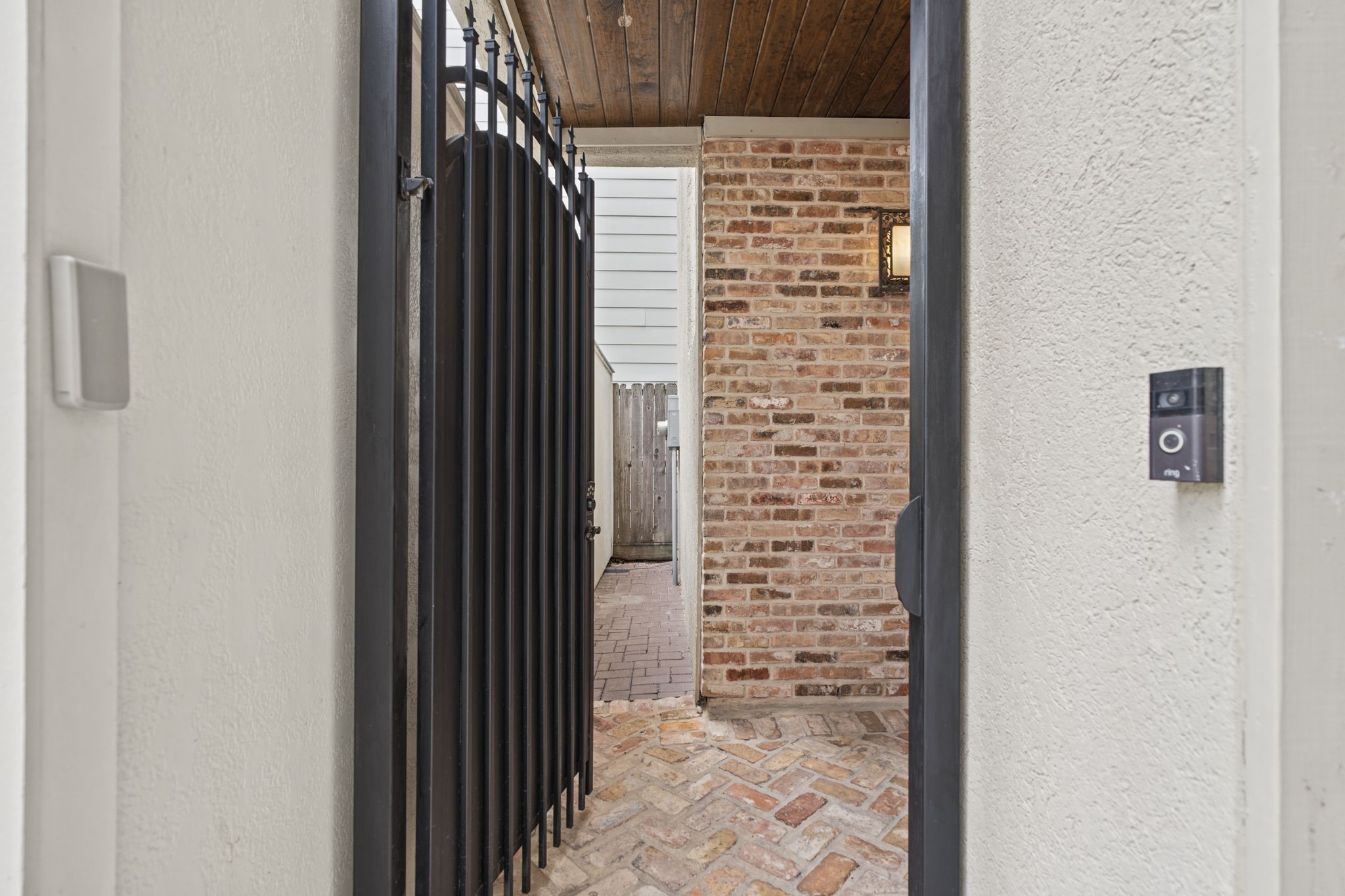 Private Entry  An elegant wrought-iron gate opens to a brick-clad entryway, where rich textures and Mediterranean architectural details create a warm and inviting first impression.