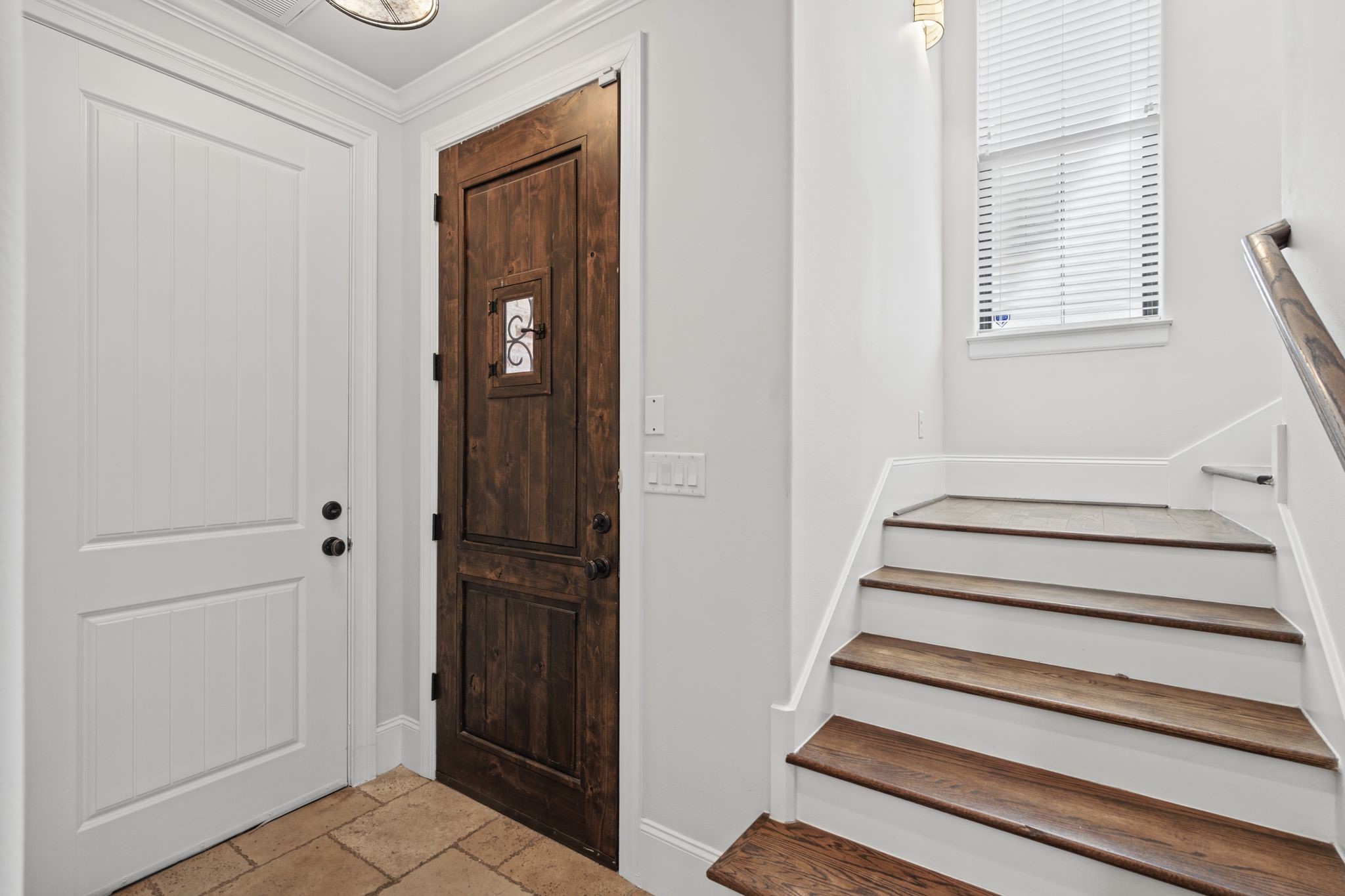 Entry [9 x 13]  First Floor. A welcoming introduction to the homes Mediterranean character, this light-filled foyer features expansive windows and a graceful staircase with solid oak treads, decorative tile risers, and wrought-iron detailing.