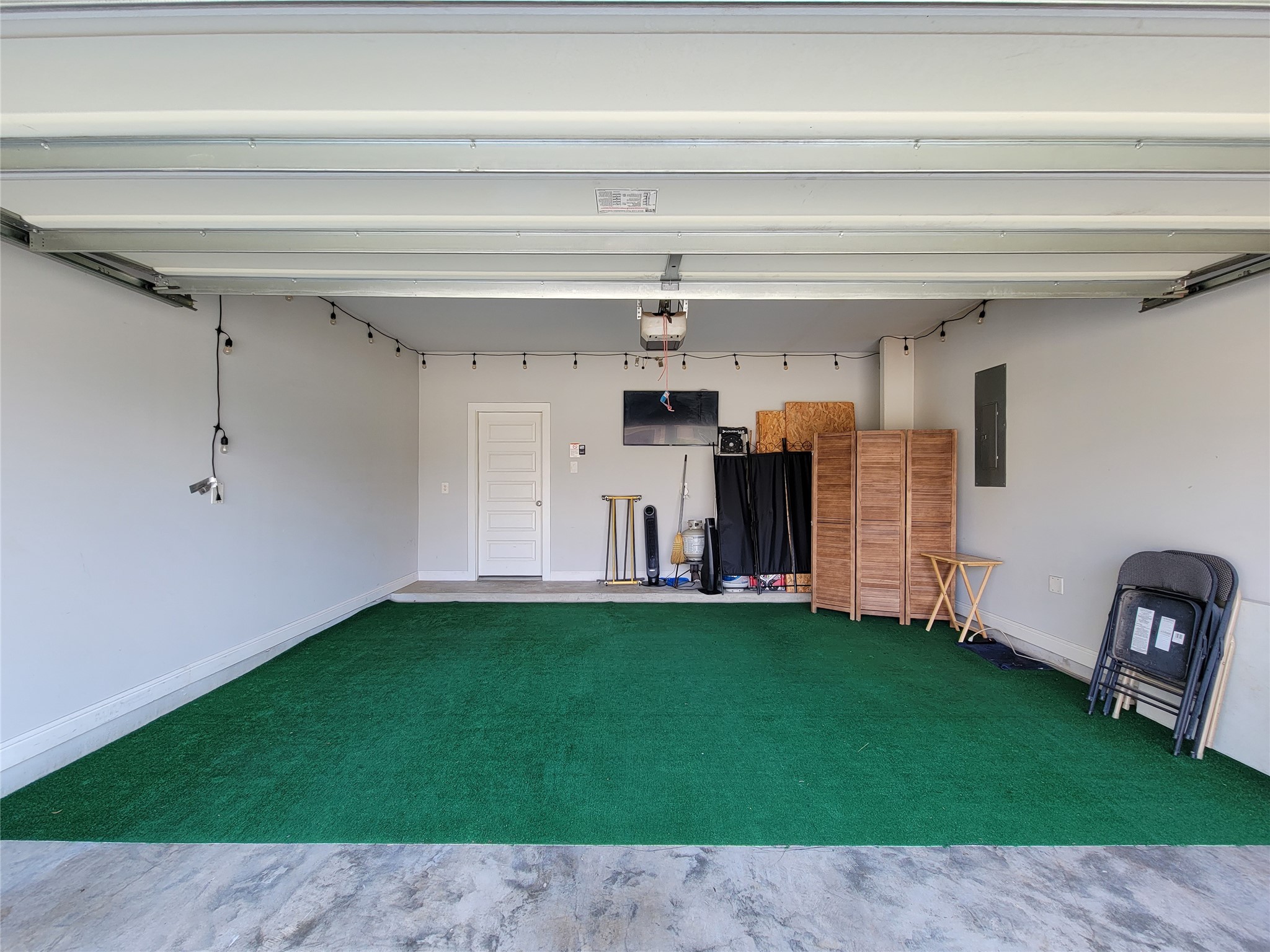 Spacious garage with artificial turf flooring, offering ample storage and versatile space for projects or hobbies.