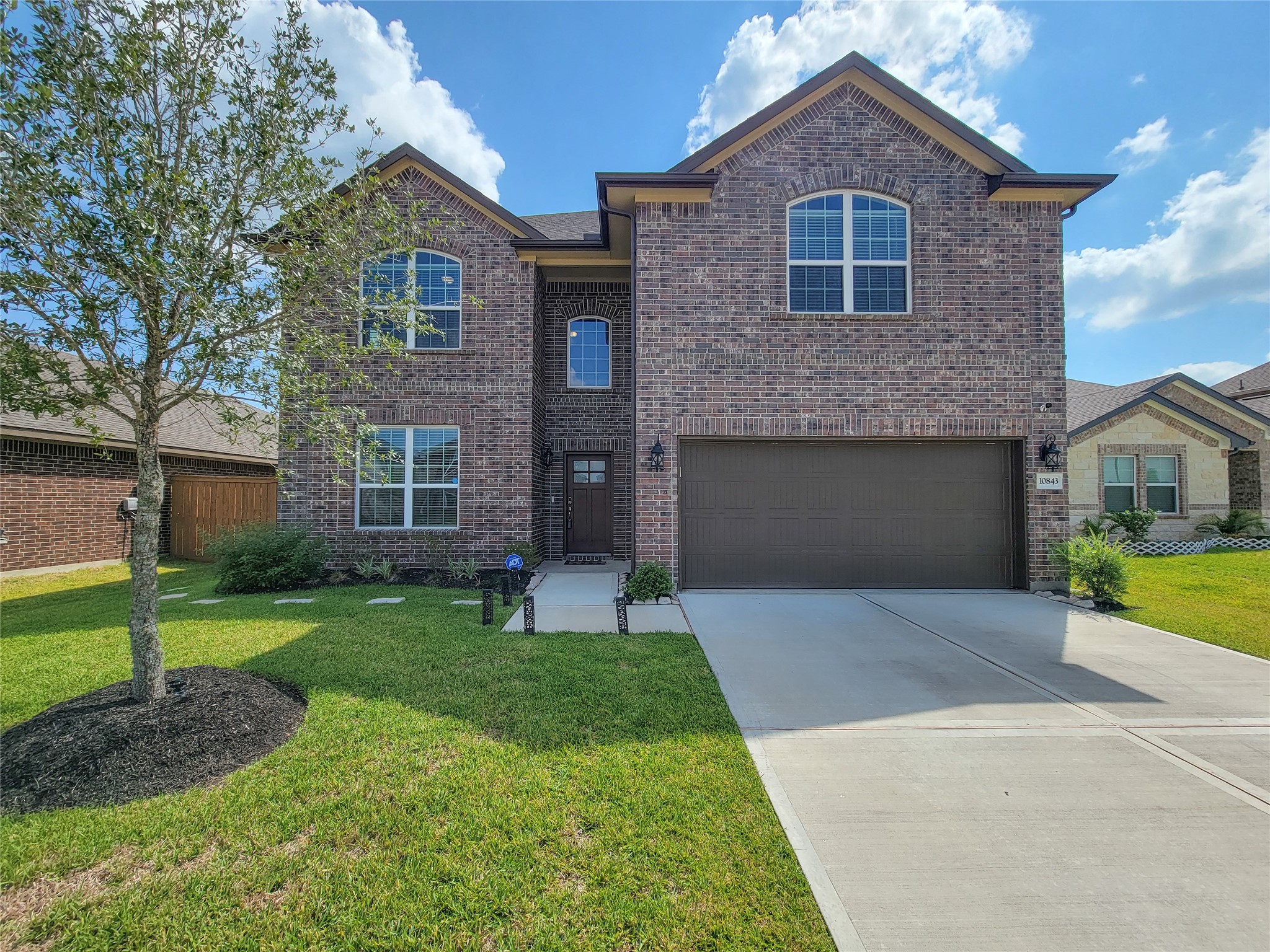 Stunning two-story brick home with a spacious driveway and attached garage, complemented by a well-maintained front lawn and charming landscaping.