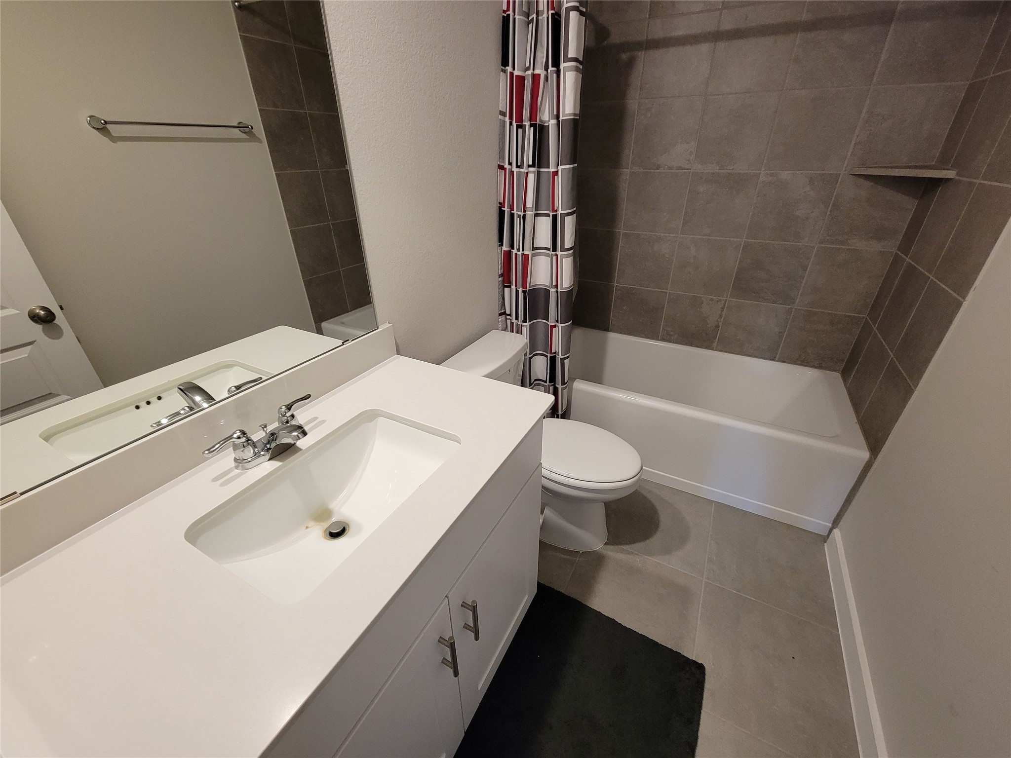 Modern bathroom with sleek white vanity, elegant tile flooring, and a stylish shower-tub combo featuring contemporary patterned curtains.