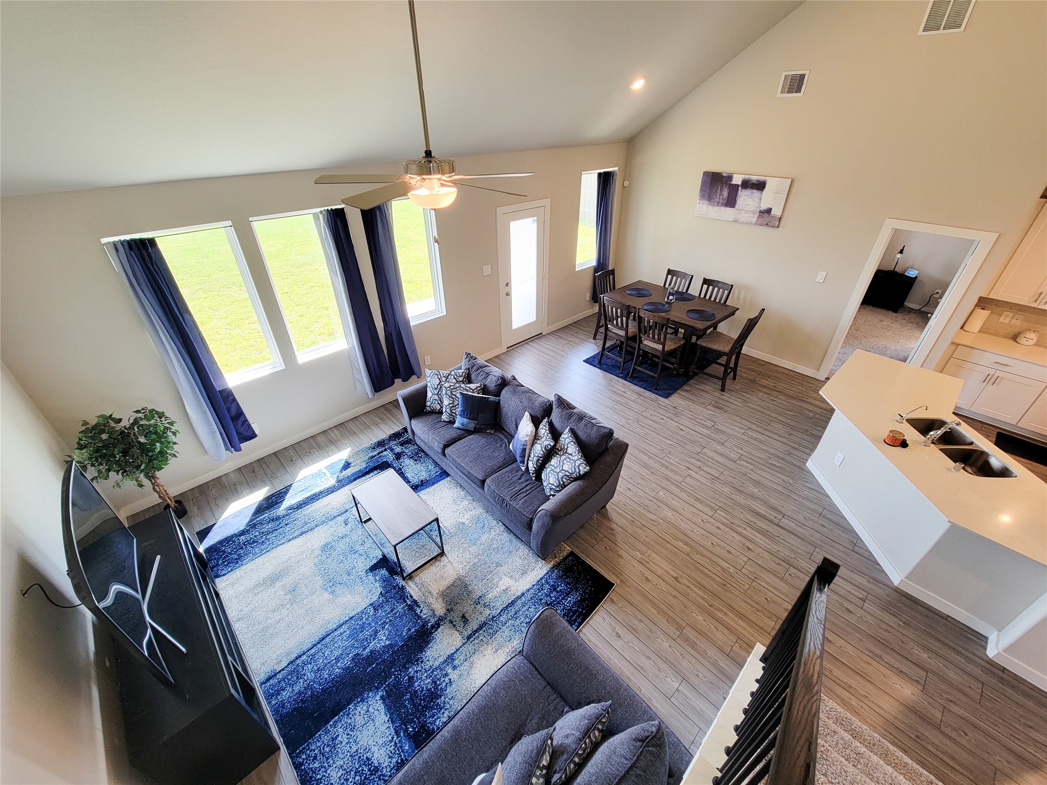 Bright and airy open-concept living space features high ceilings, stylish wood flooring, and large windows that flood the room with natural light. The modern kitchen with a breakfast bar seamlessly connects to the cozy living area, perfect for entertaining.