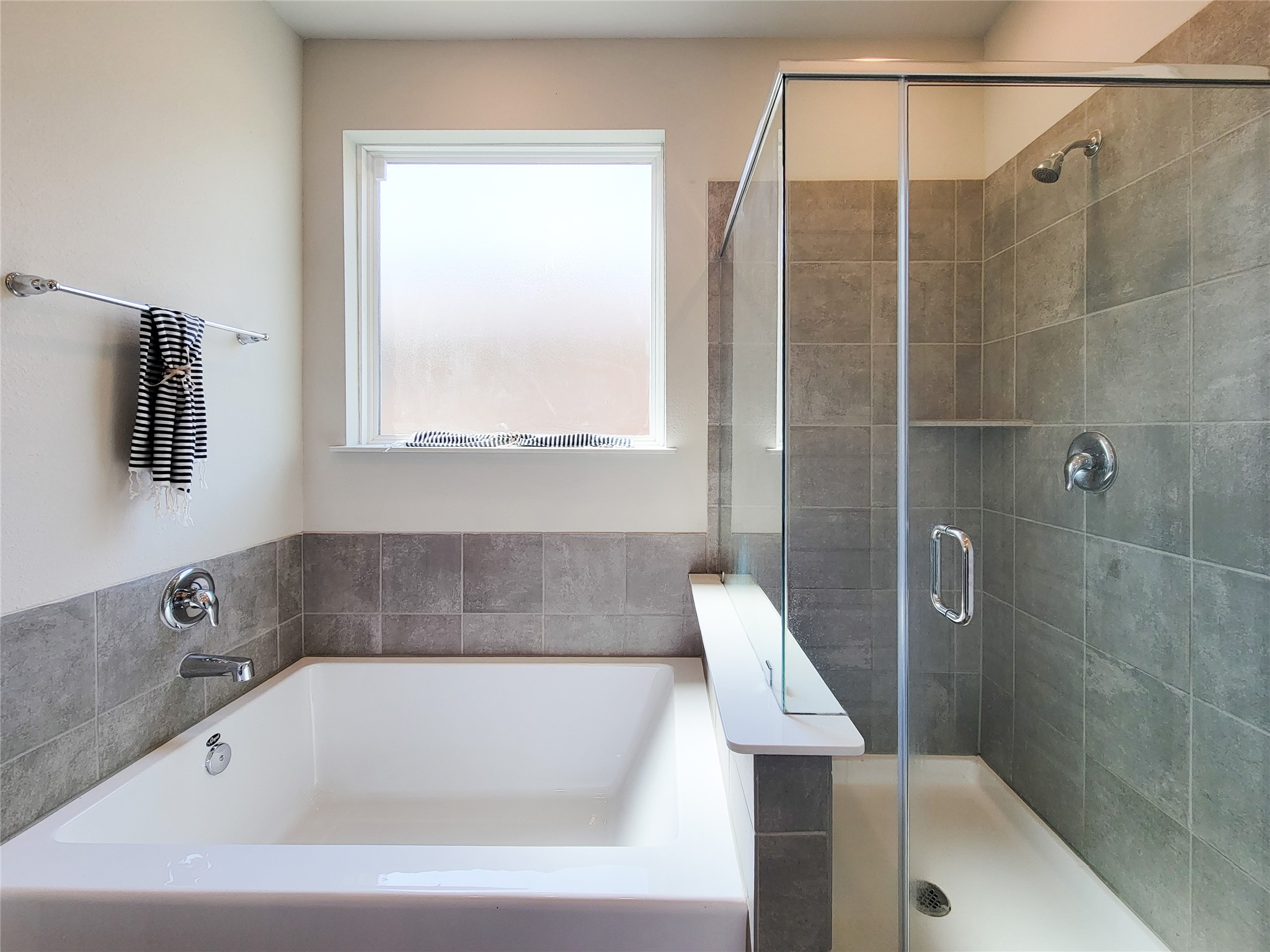 Luxurious bathroom featuring a large soaking tub and a sleek glass-enclosed shower, accented with elegant gray tiles.