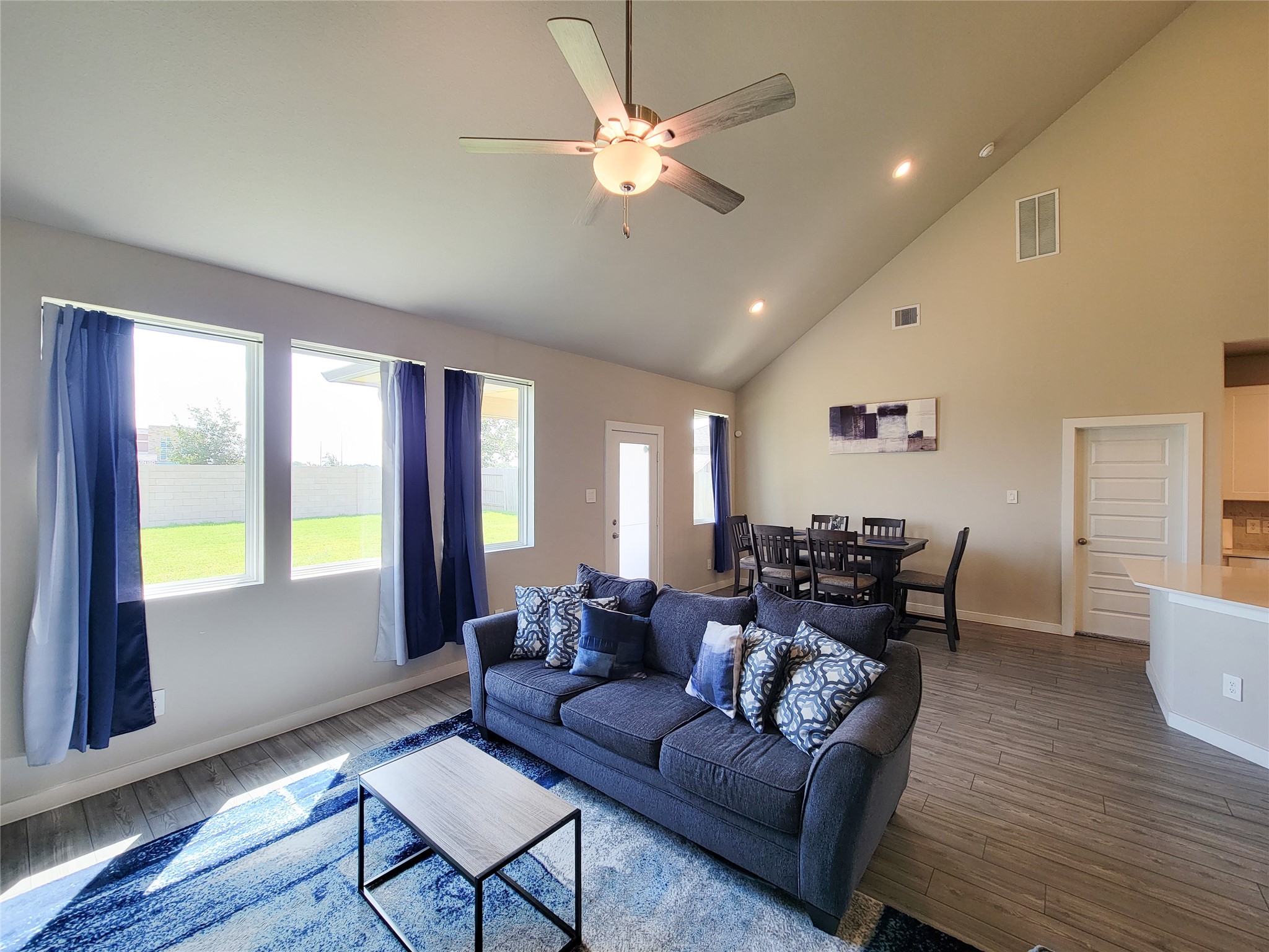 Spacious living area with high ceilings and abundant natural light, featuring a comfortable seating arrangement and adjacent dining space, perfect for entertaining.
