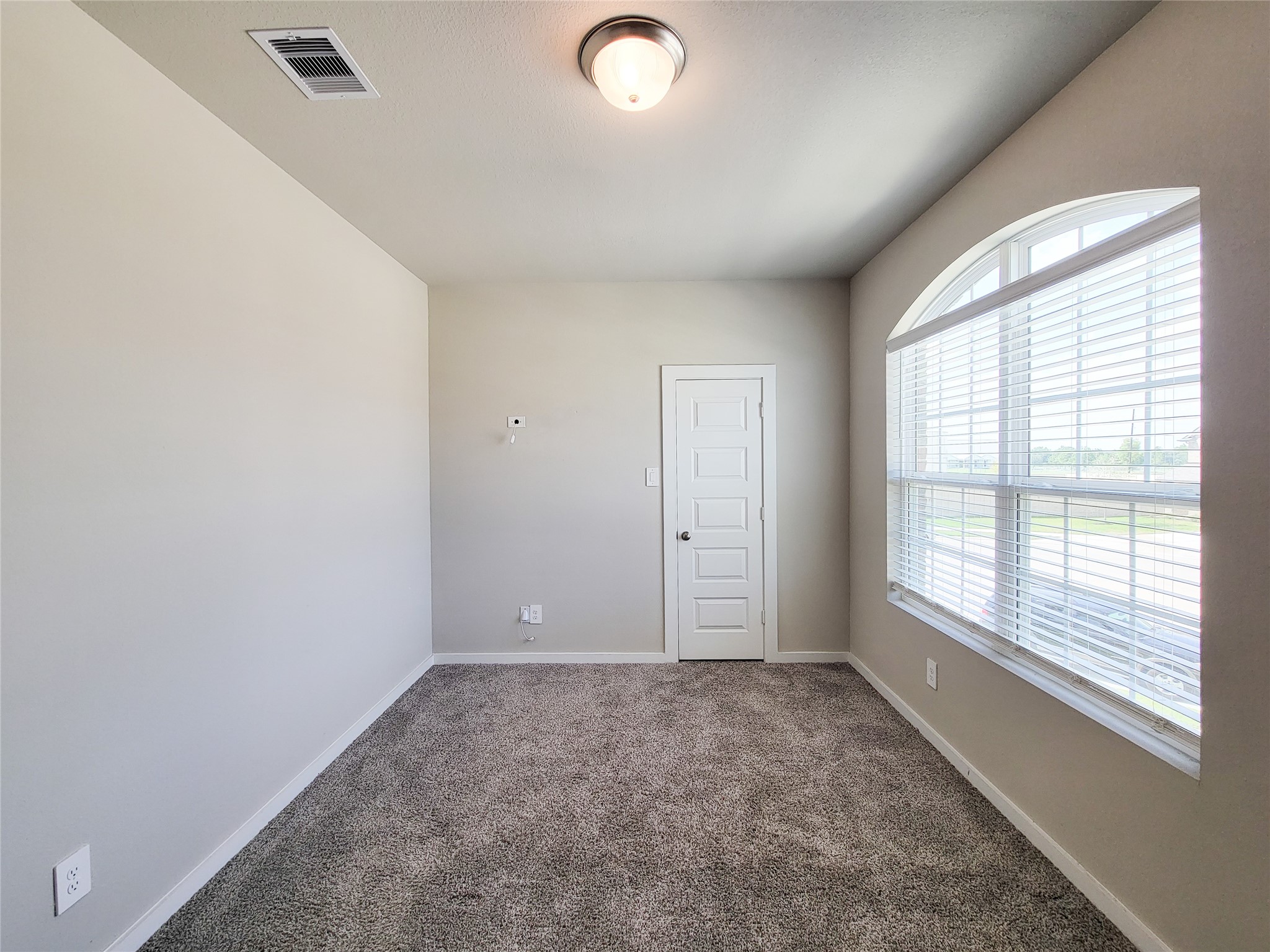 Bright and cozy room featuring plush carpeting, a large arched window for ample natural light, and a modern light fixture, perfect for a home office or guest bedroom.
