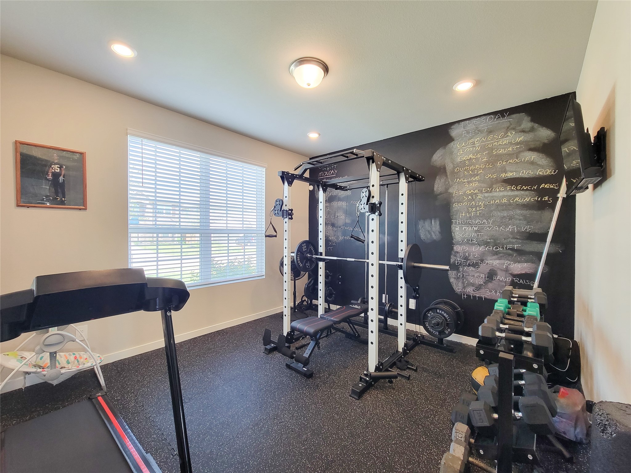 Bright and functional home gym featuring a versatile workout station, dumbbell rack, treadmill, and a motivational chalkboard wall.