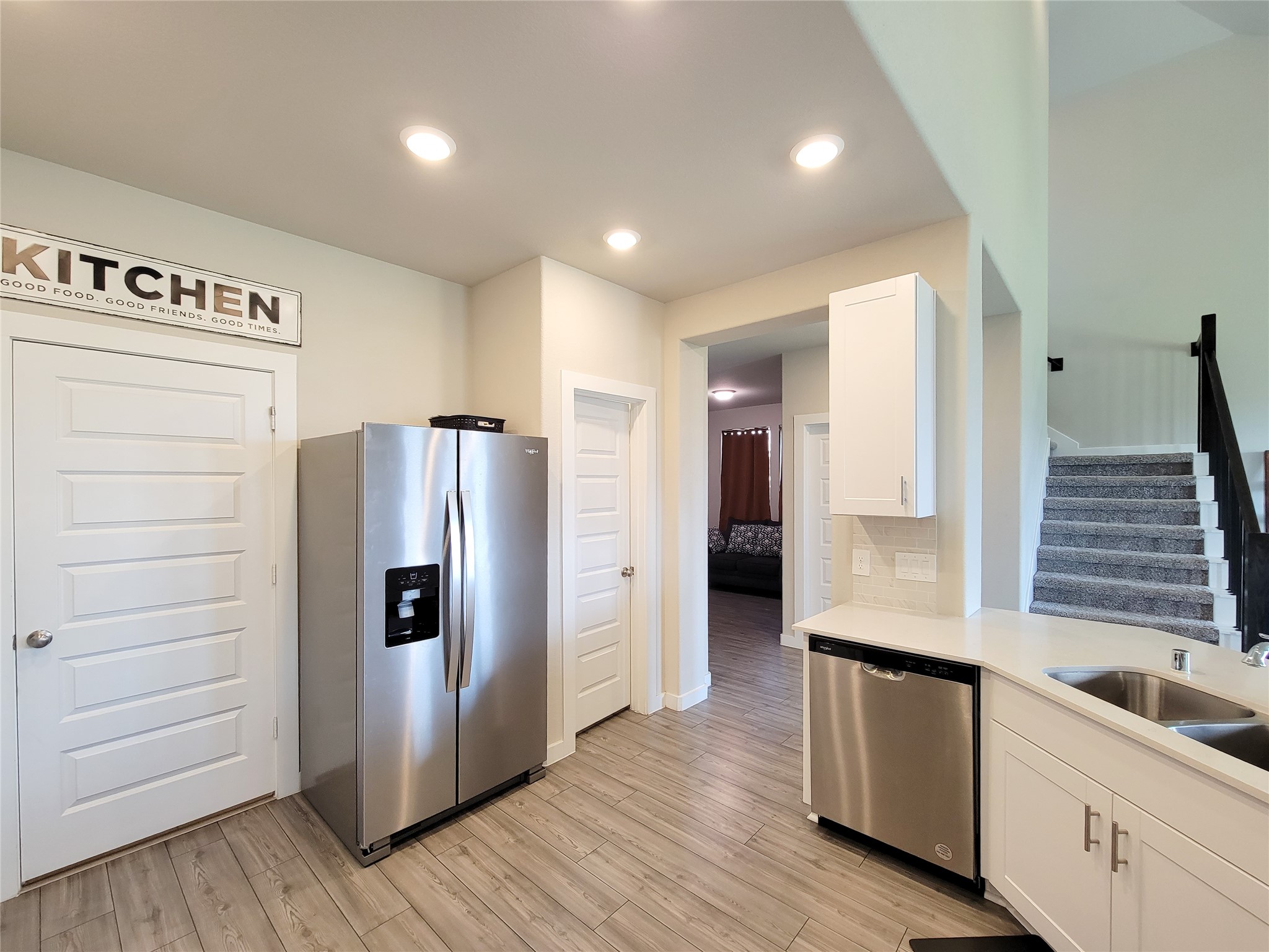 Modern kitchen with stainless steel appliances, ample cabinetry, and sleek wood flooring, leading to a cozy living area and carpeted staircase.