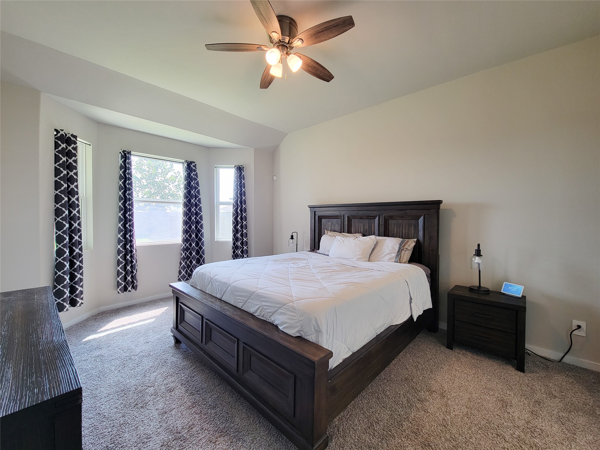 Spacious bedroom with plush carpeting, a large window for natural light, and a ceiling fan for comfort.