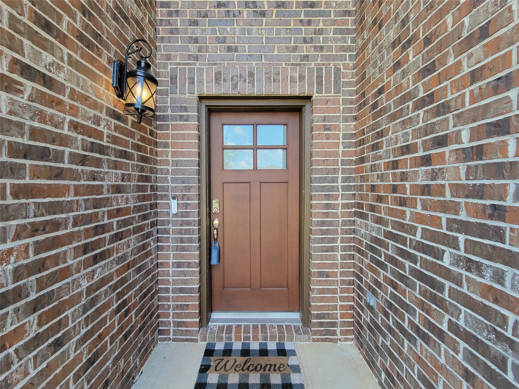 Charming brick entryway with a classic wooden door and a welcoming lantern sconce, complemented by a cozy doormat.