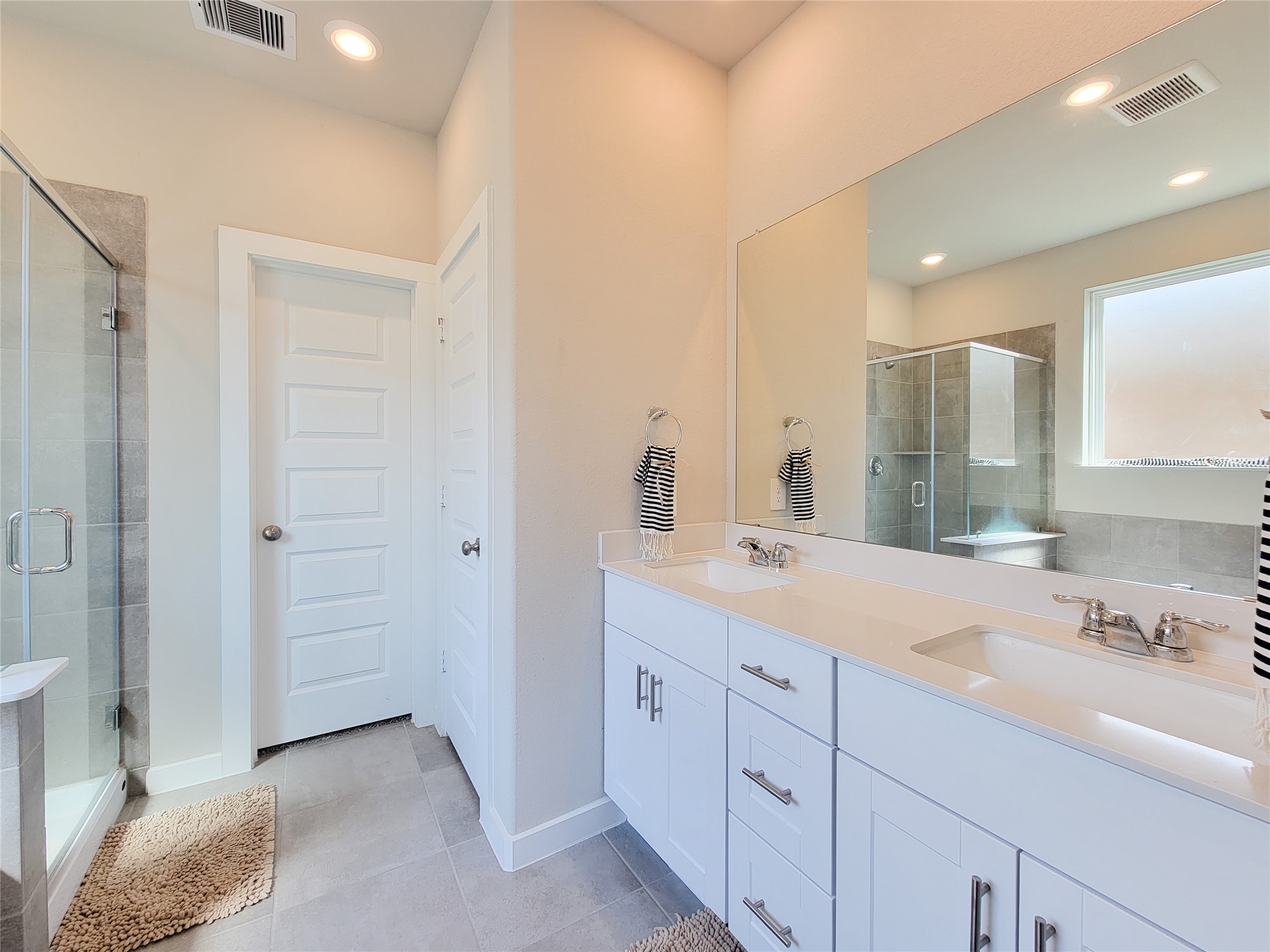 Bright and modern bathroom featuring double sinks, a large mirror, and a spacious glass-enclosed shower, complemented by elegant fixtures and neutral tile flooring.