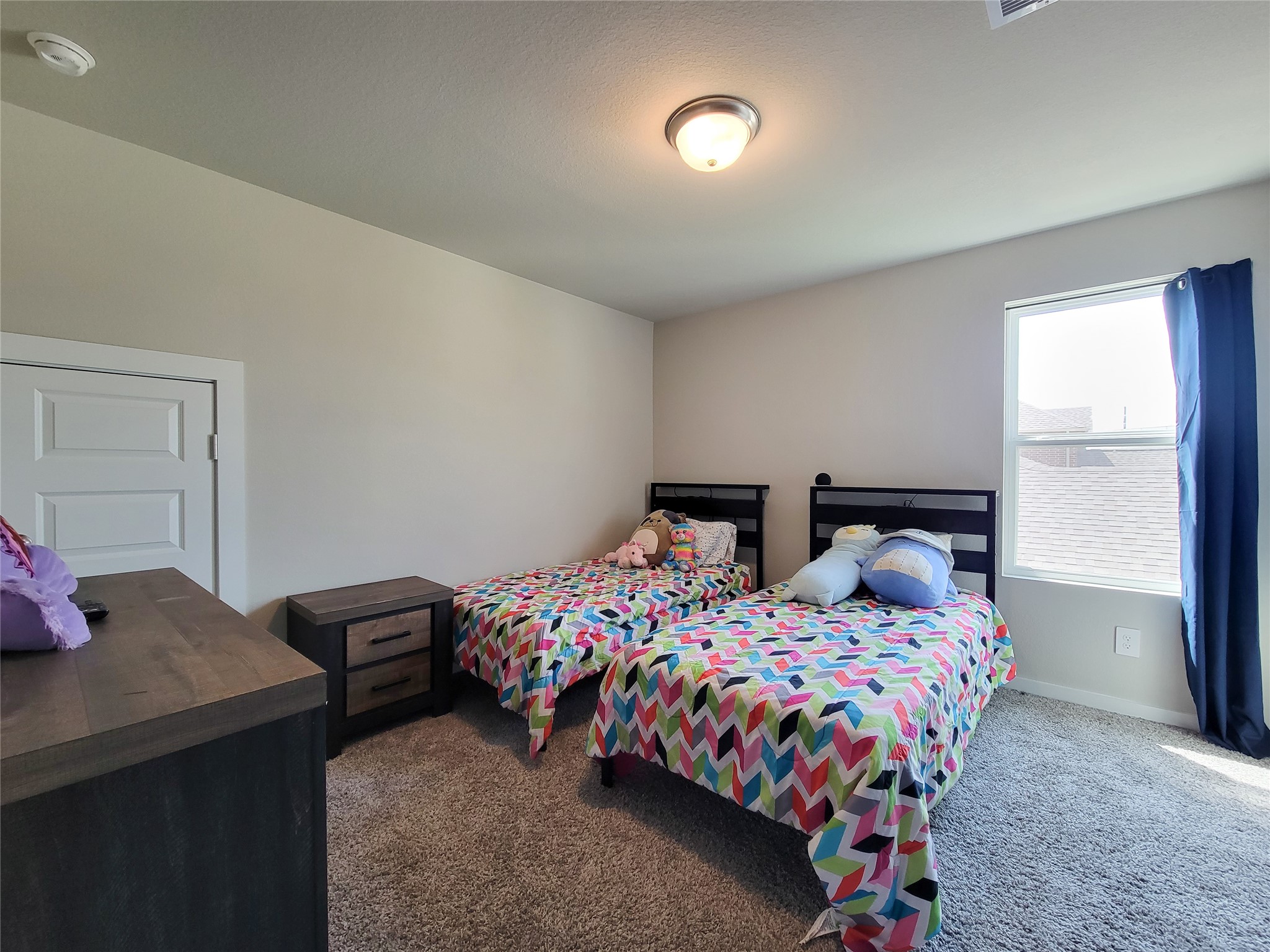 Cozy bedroom featuring twin beds with colorful bedding, plush carpet, and ample natural light from a large window, creating a warm and inviting atmosphere.