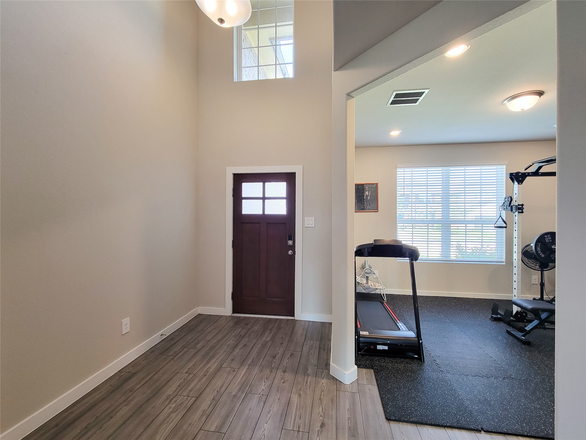 Inviting entryway with high ceilings and elegant flooring, leading to a bright home gym filled with natural light.