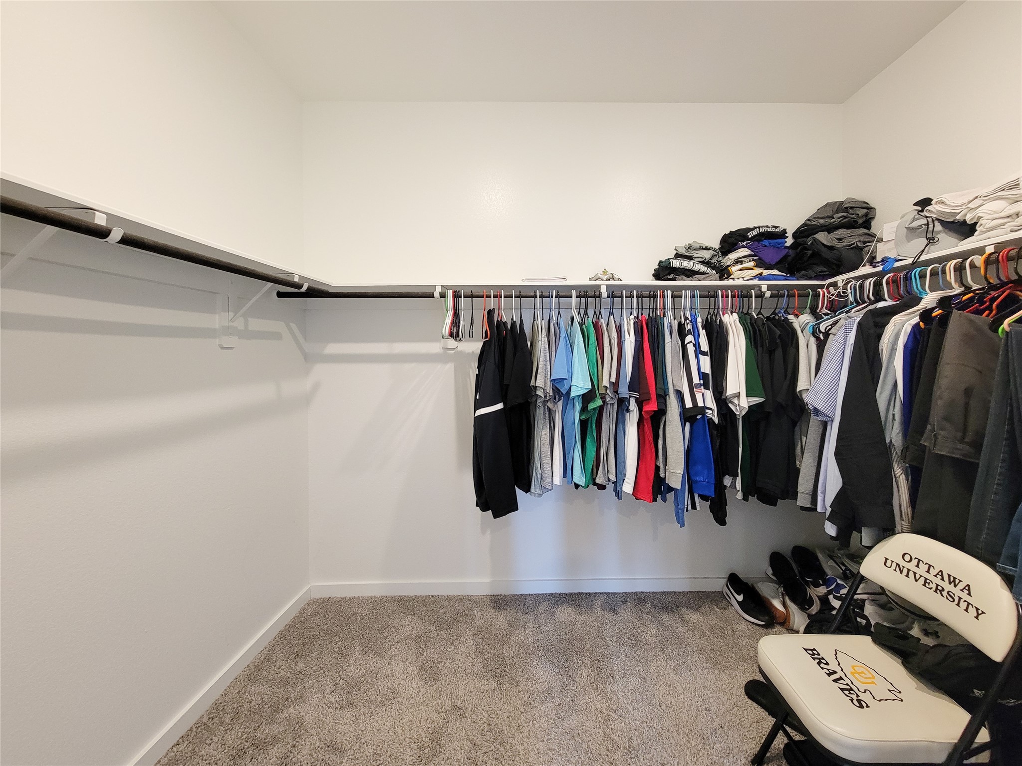 Spacious walk-in closet with ample hanging space, shelving, and soft carpet flooring, perfect for organizing your wardrobe.