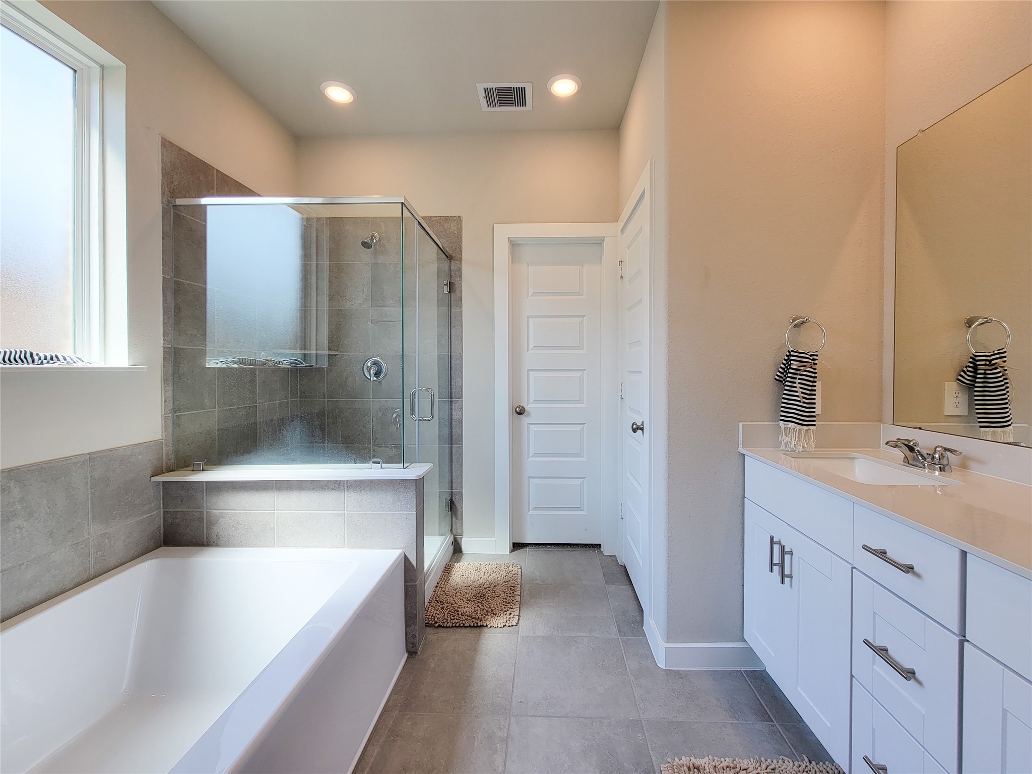 Elegant bathroom featuring a spacious glass-enclosed shower, a sleek bathtub, and a modern vanity with ample storage and a large mirror.
