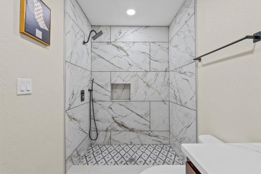 Renovated full bathroom with new cabinets, and quartz countertops. Accessories include a rainfall shower head and upgraded faucets.