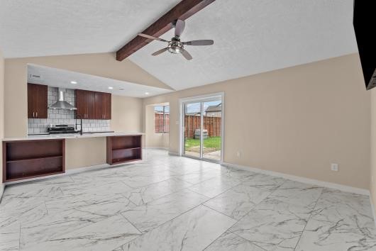 This spacious living area features a vaulted ceiling with an exposed beam and a ceiling fan. It has large marble-patterned tiles, with an open concept to the kitchen .with Sliding glass doors provide access to a fenced backyard, offering plenty of natural light. This spacious living area features a vaulted ceiling with an exposed beam and a ceiling fan. It has large marble-patterned tiles, with an open concept to the kitchen .with Sliding glass doors provide access to a fenced backyard, offering plenty of natural light.