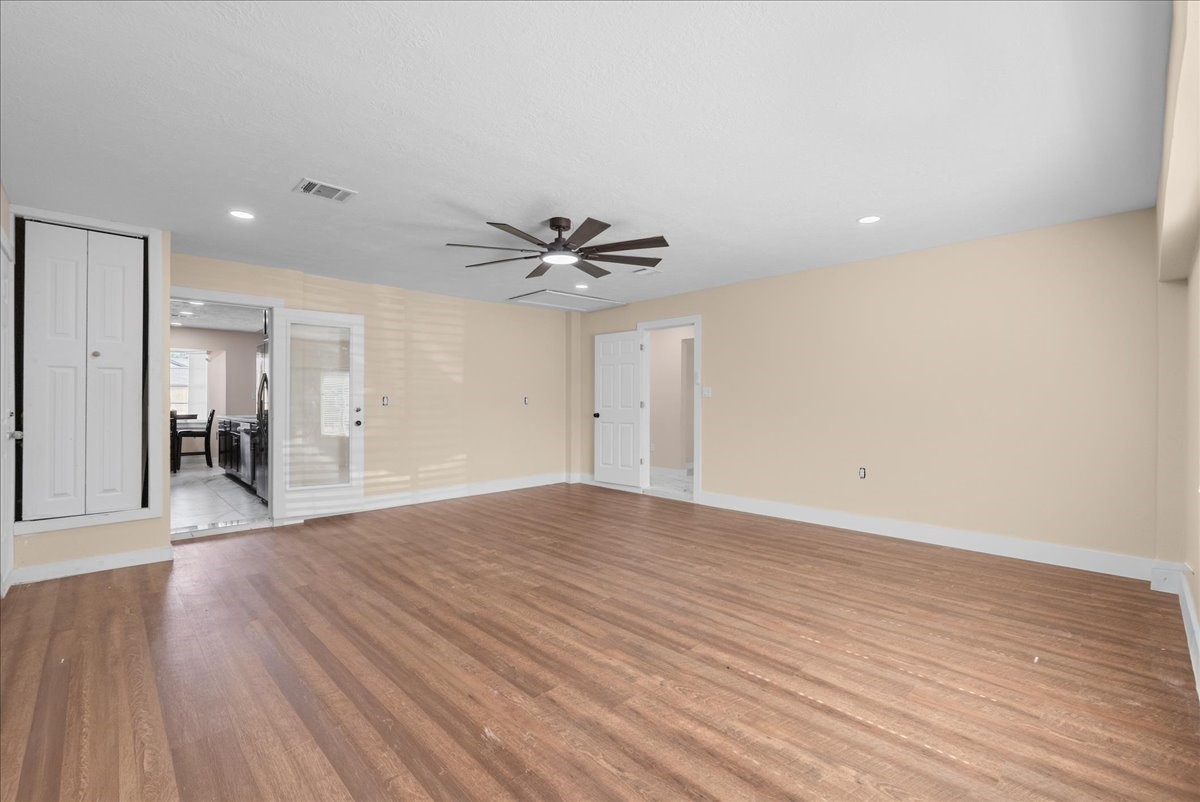 Flex room with wood like floor, ceiling fan, looking back into kitchen area.