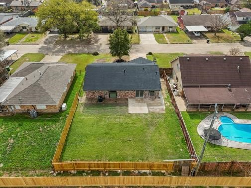 This aerial photo shows a single-story brick house with a new roof, located in a suburban neighborhood. It features a spacious, fenced backyard with a large patio.