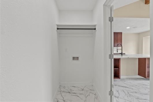 This photo shows a small, tiled laundry area with a hook-up for appliances, adjacent to an open kitchen space.