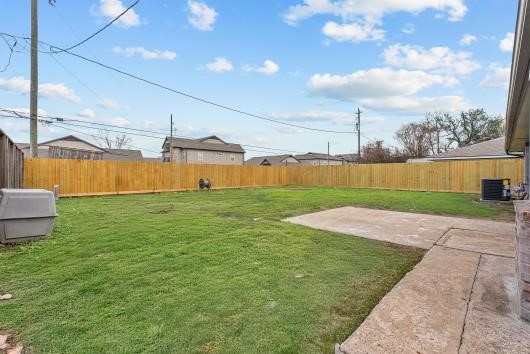 This photo showcases a spacious backyard with a well-maintained lawn, surrounded by a wooden fence for privacy. A concrete patio area offers space for outdoor activities or entertaining.