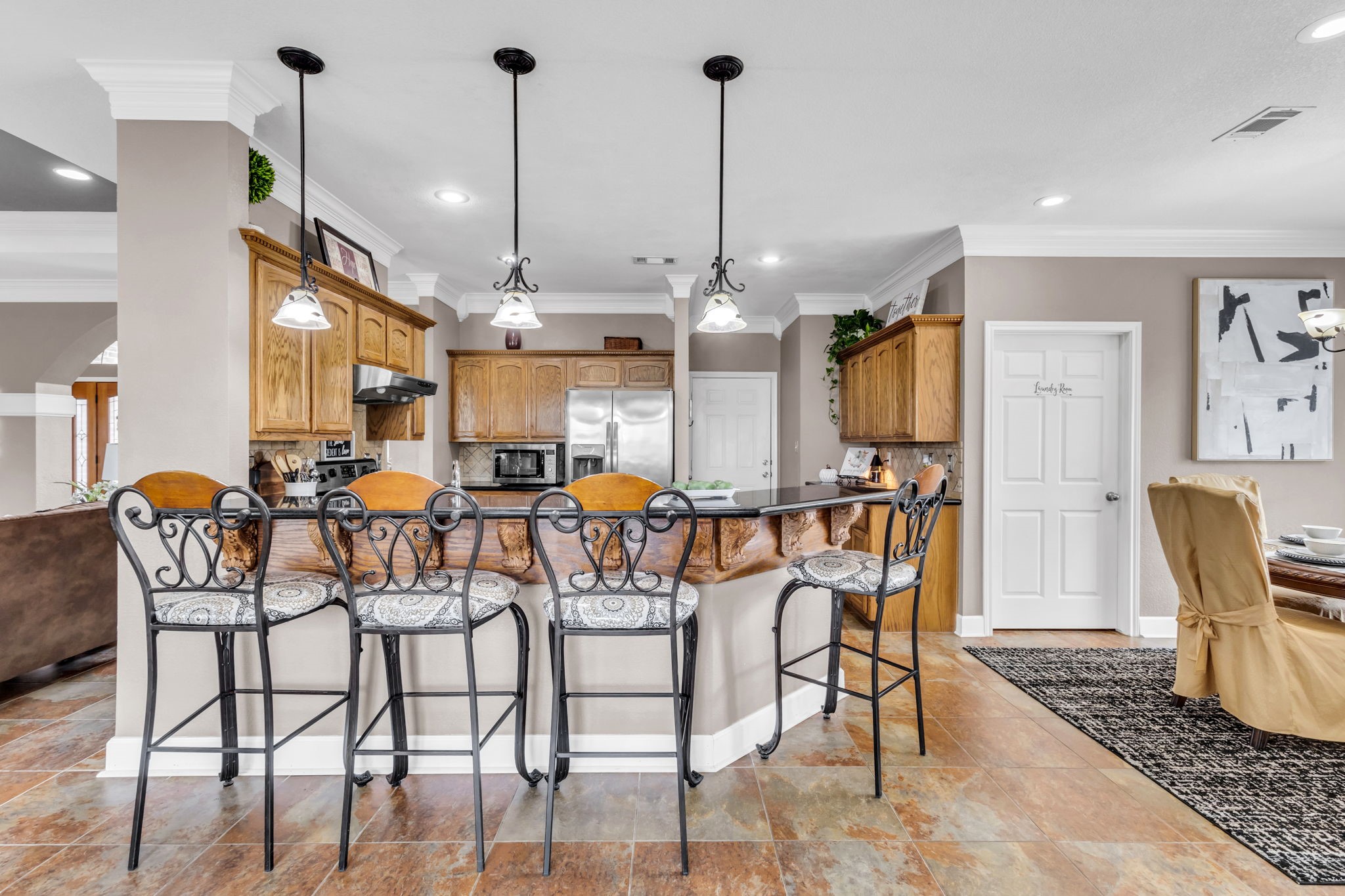 Spacious kitchen featuring a large breakfast bar, abundant wood cabinetry, and decorative pendant lighting. The open design connects seamlessly to the living and dining areas, ideal for everyday living and entertaining.
