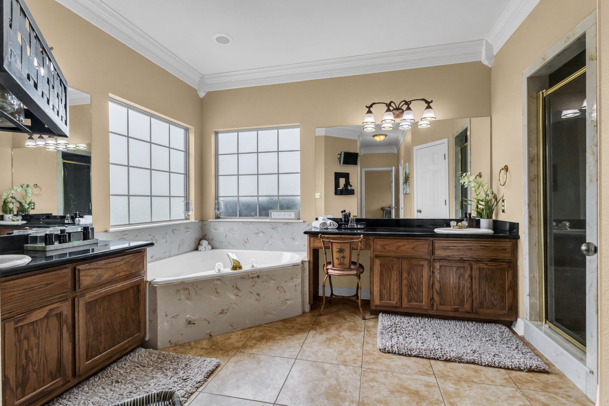 Spacious primary bathroom featuring separate vanities, a relaxing soaking tub surrounded by windows, a separate glass-enclosed shower, and plenty of cabinet space. A comfortable and functional layout for everyday convenience.