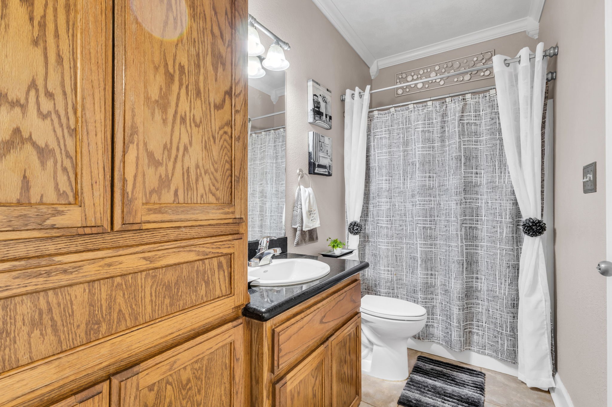 Adjoining guest bathroom features a tub and shower combination, wood cabinetry, dark countertop, and additional built-in storage for everyday convenience.