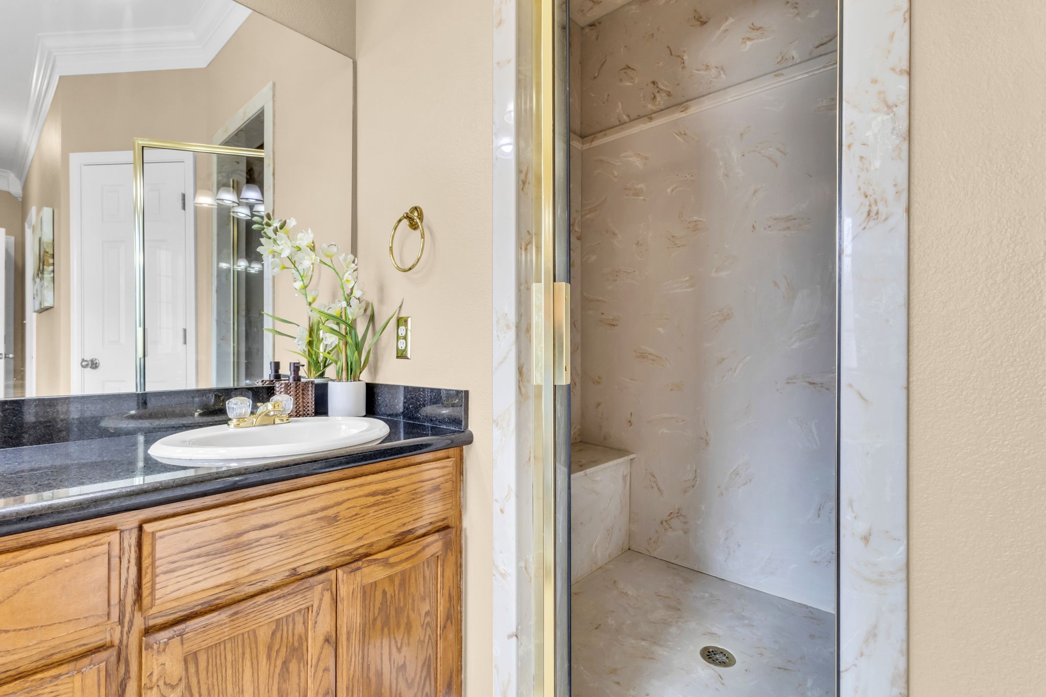 Primary bathroom features a separate glass-enclosed shower with built-in bench, decorative surround, and spacious vanity with dark countertops and ample cabinet storage.