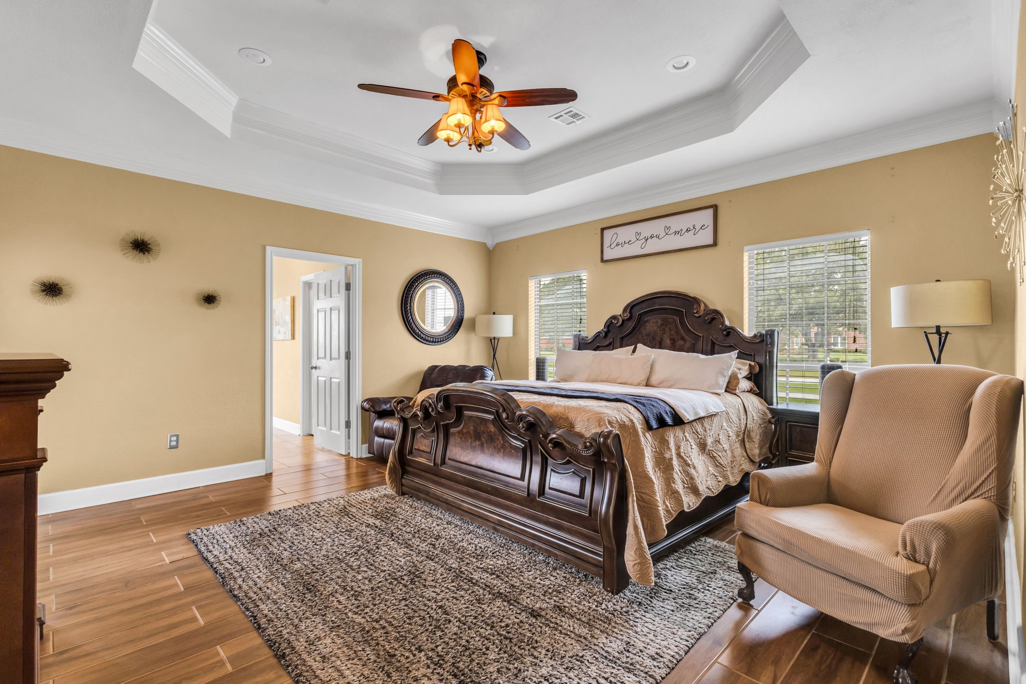 Spacious primary bedroom featuring a tray ceiling with crown molding, wood-look tile flooring, and large windows that bring in natural light. Plenty of room for additional furnishings and a comfortable sitting area.