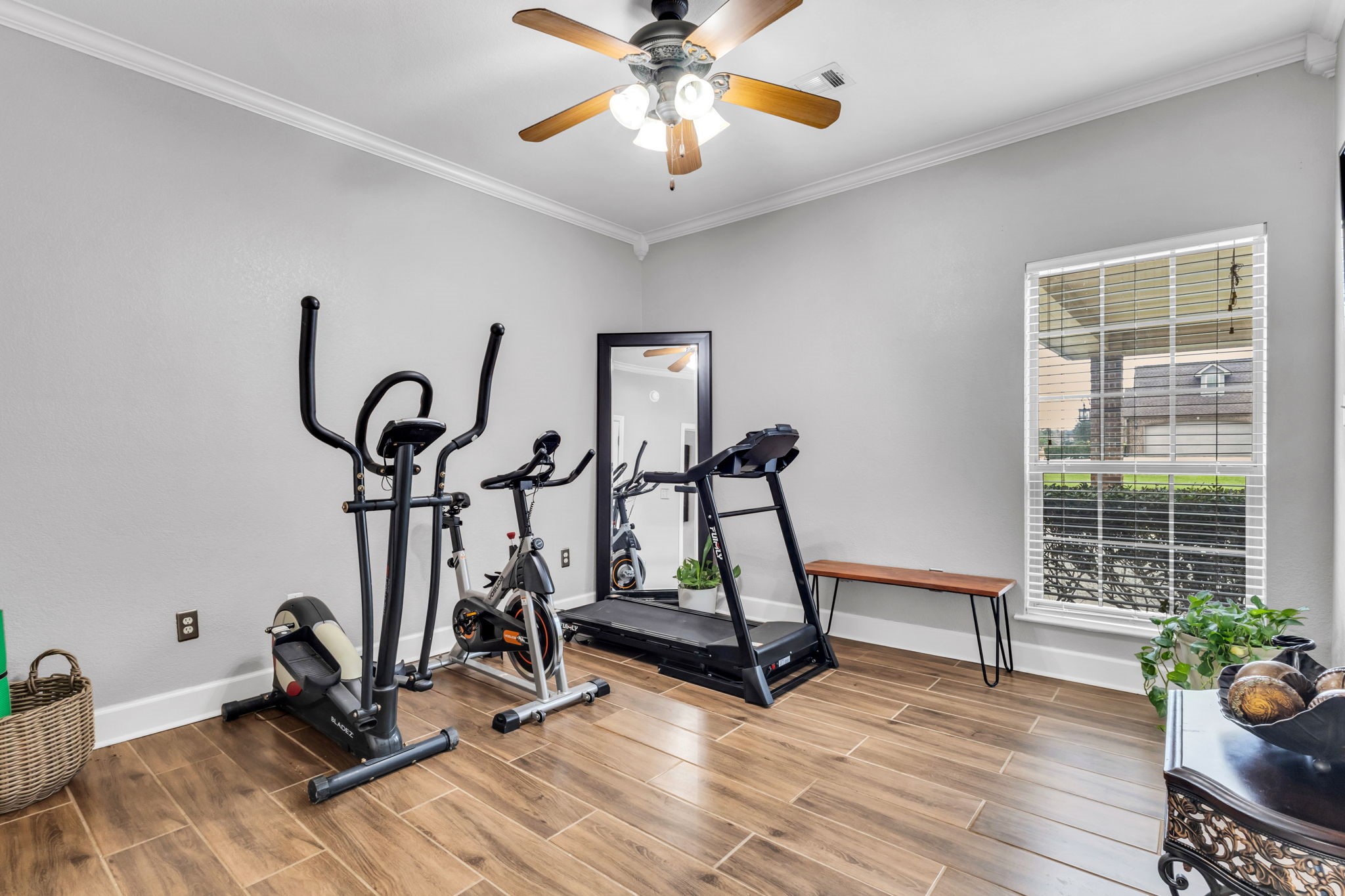 Versatile second guest bedroom currently used as a home gym, featuring wood-look flooring, crown molding, ceiling fan, and natural light. This flexible space can easily accommodate a variety of needs.