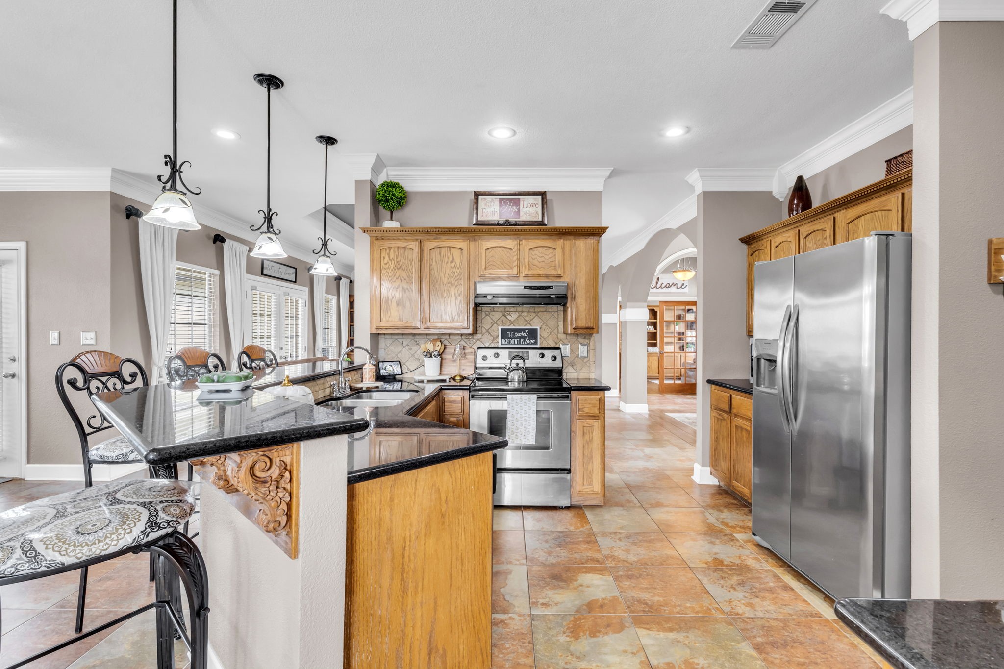 Additional kitchen view showcasing expansive dark countertops, rich wood cabinetry, decorative tile backsplash, and a functional layout with generous counter space. Recessed lighting and crown molding add a polished touch to this inviting space.