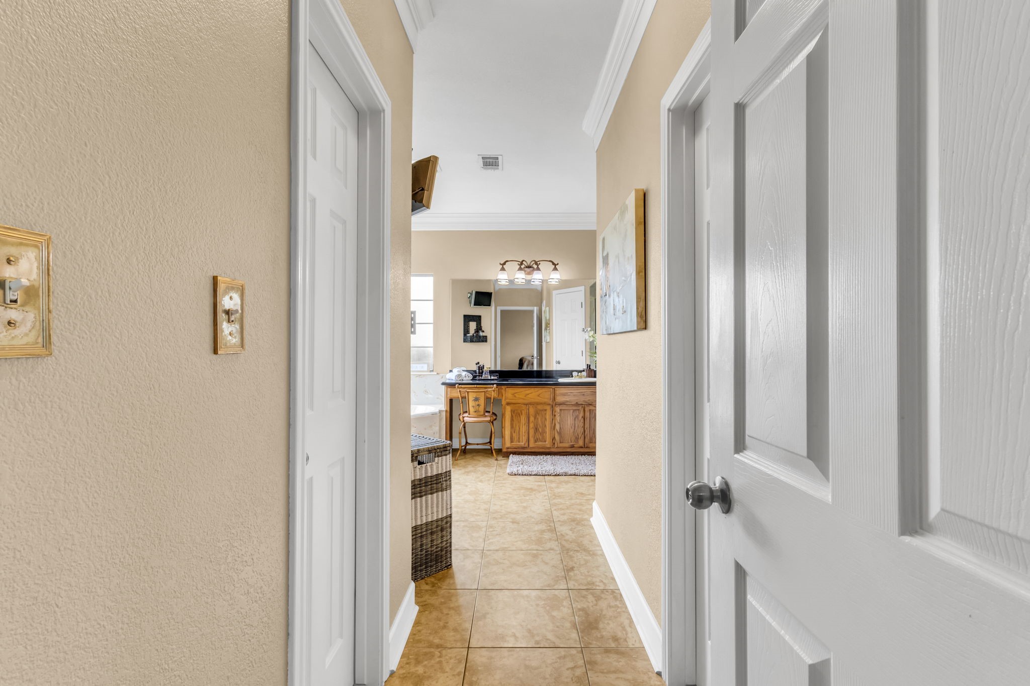 Private entry to the primary bathroom featuring tile flooring, crown molding, and convenient access to the vanity and adjoining his/her walk in closets.