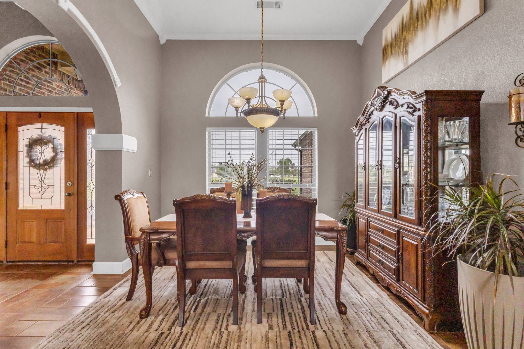Formal dining room featuring high ceilings, an elegant lighting, arched window, and decorative architectural details. Conveniently located just off the entryway, offering a welcoming space for gatherings and entertaining.