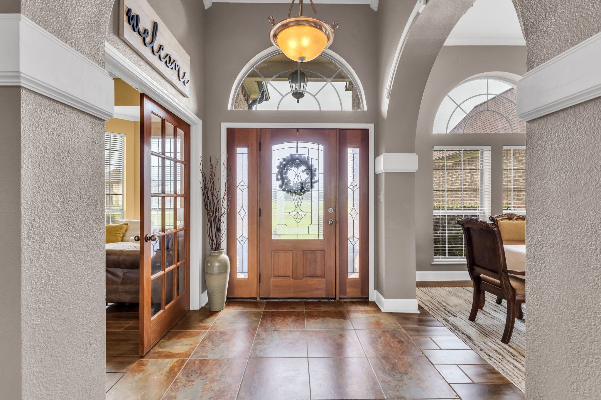 Inviting entryway featuring decorative tile flooring, high ceilings, arched windows, and elegant architectural details. French doors lead to a separate room, while an open archway provides access to the formal dining area.