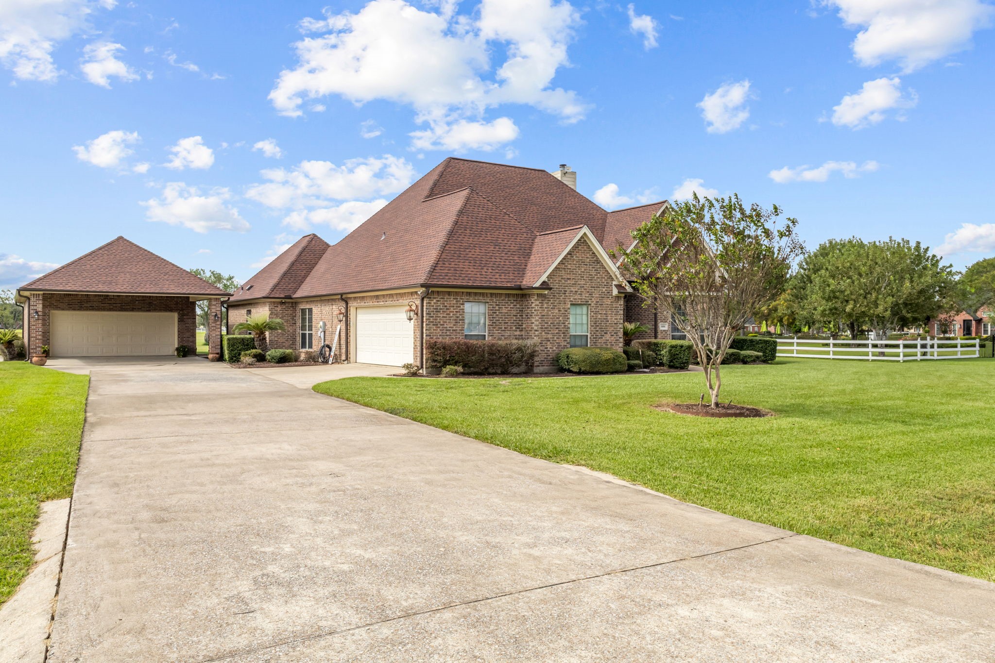 Side view highlighting the extended concrete driveway, attached garage, and additional detached two-car garage, providing ample parking space and convenient access.