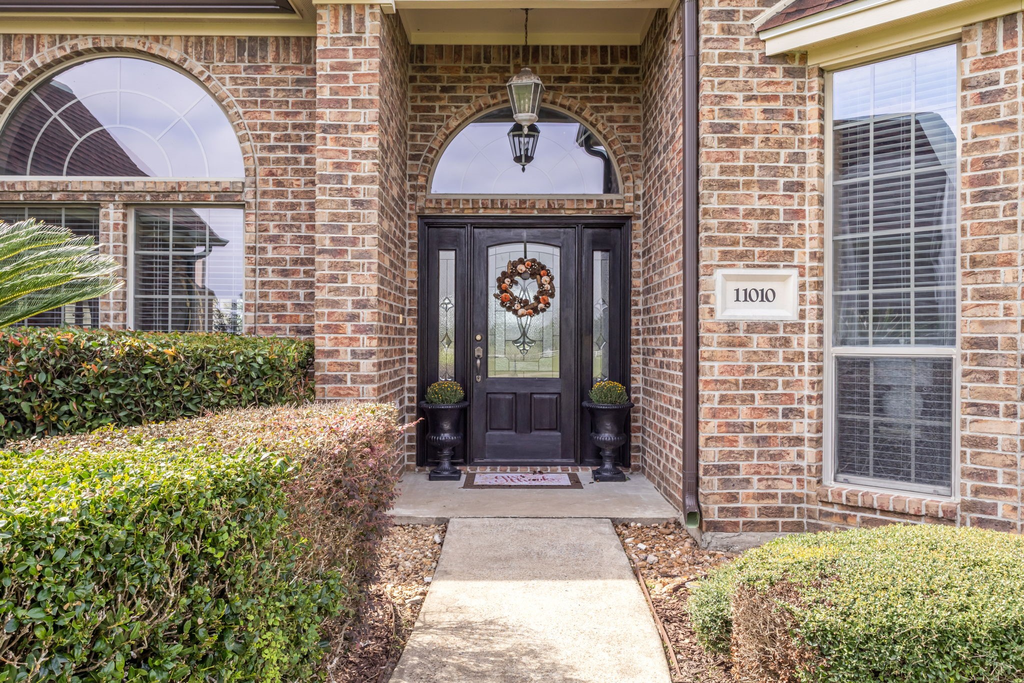 Welcoming covered front entry featuring an elegant glass-paneled door with decorative sidelights, arched windows, and beautifully maintained landscaping.
