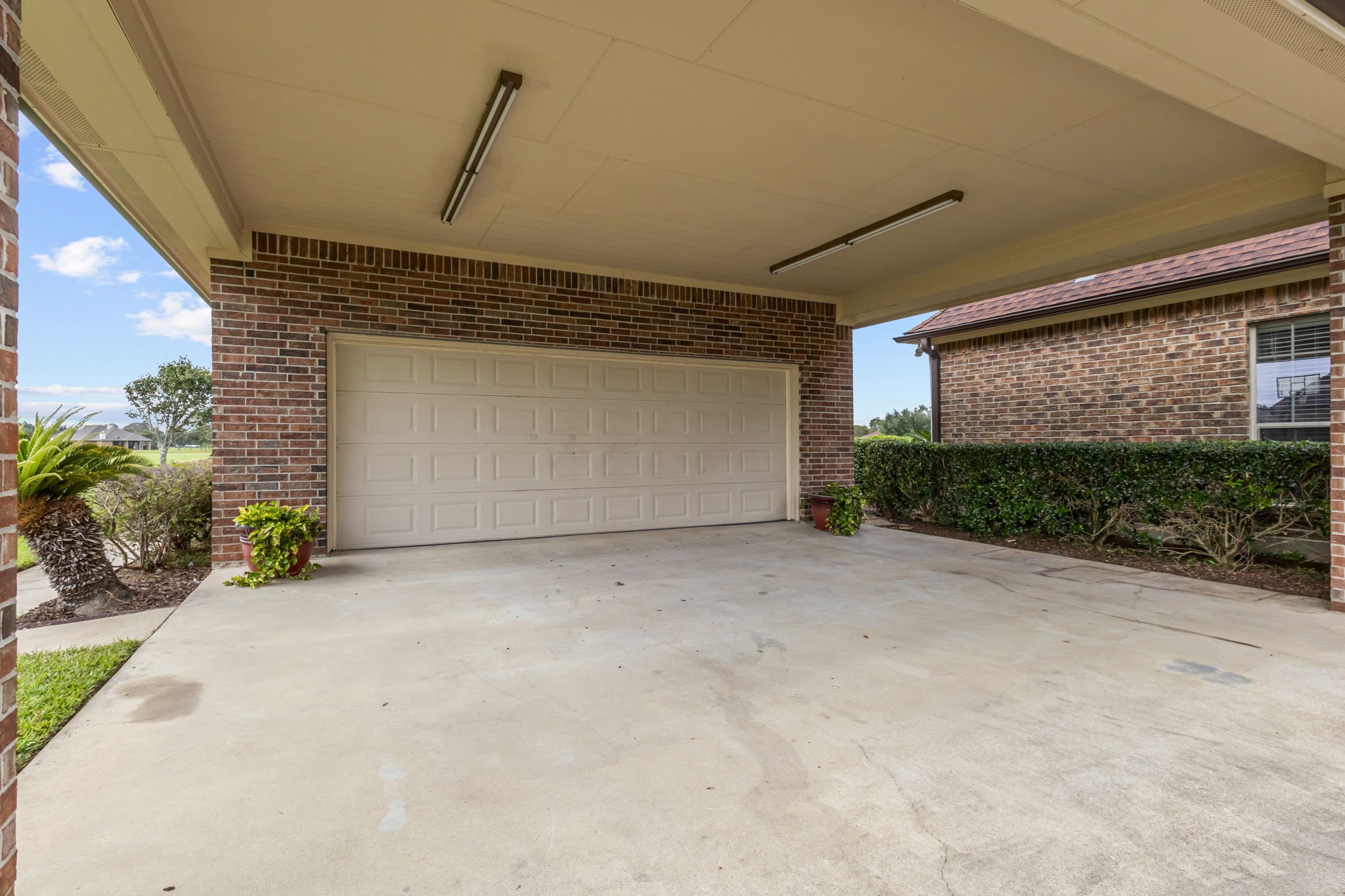 Spacious detached two-car garage with an expansive covered concrete carport parking area, overhead lighting, and convenient access. The brick exterior and surrounding landscaping complement the home's overall appeal.