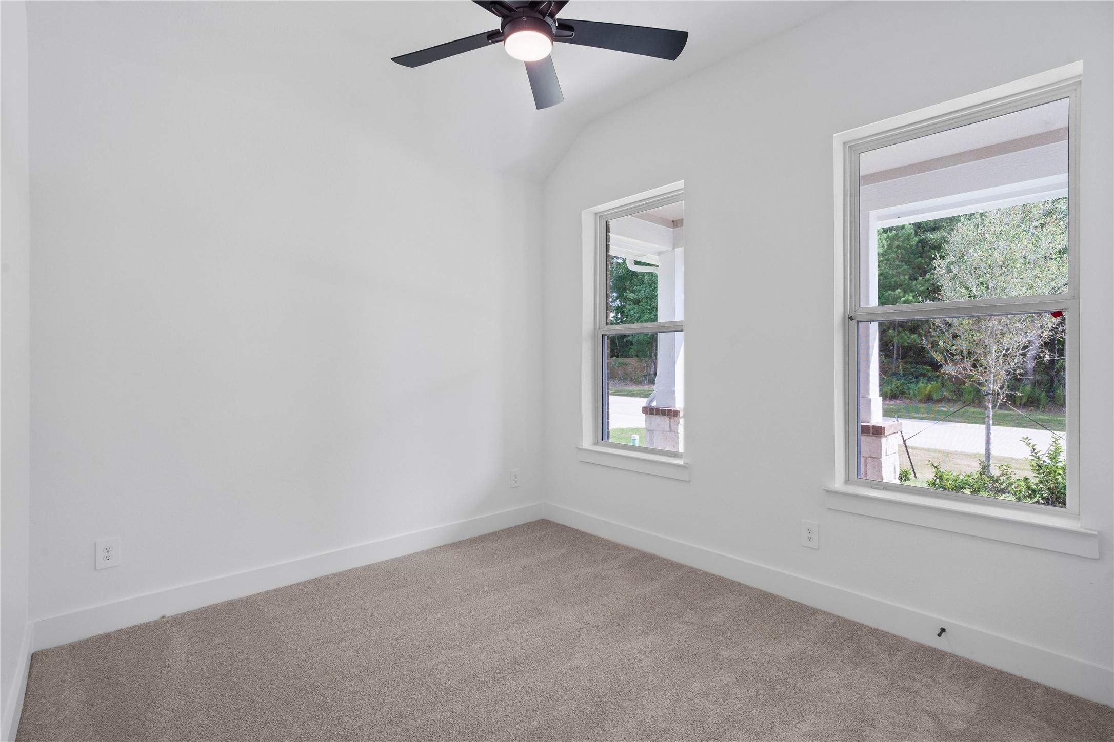 This bright secondary bedroom is situated at the front of the home, offering beautiful street-facing views that fill the space with natural light. It features large windows, plush carpet flooring, sloped high ceilings with ceiling fan, and an ample sized closet.