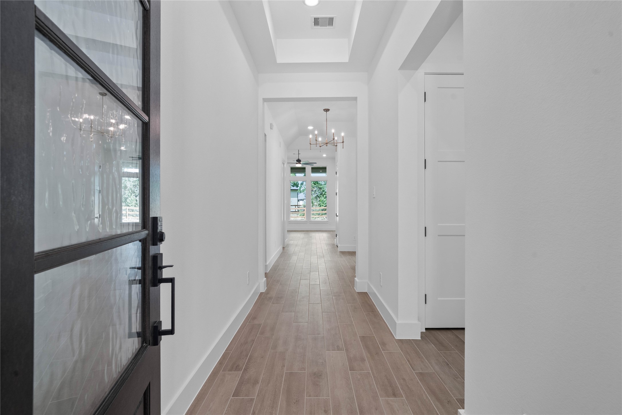 A bright, elongated foyer features a grand recessed tray ceiling and warm wood tile flooring that instantly establishes a welcoming, inviting atmosphere upon entry.